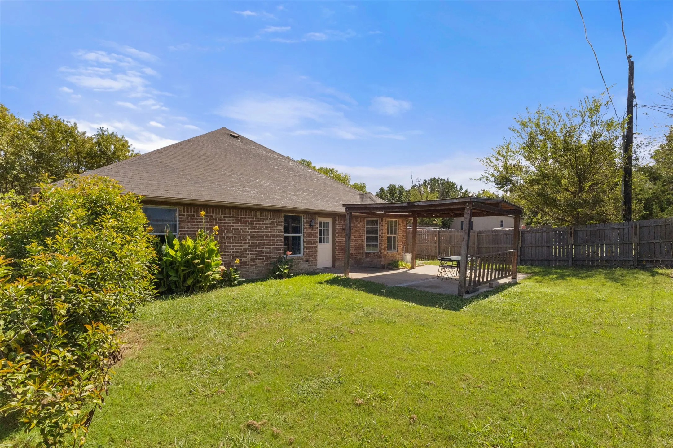 Rear view of property featuring a patio area, brick siding, a fenced backyard, and a shingled roof
