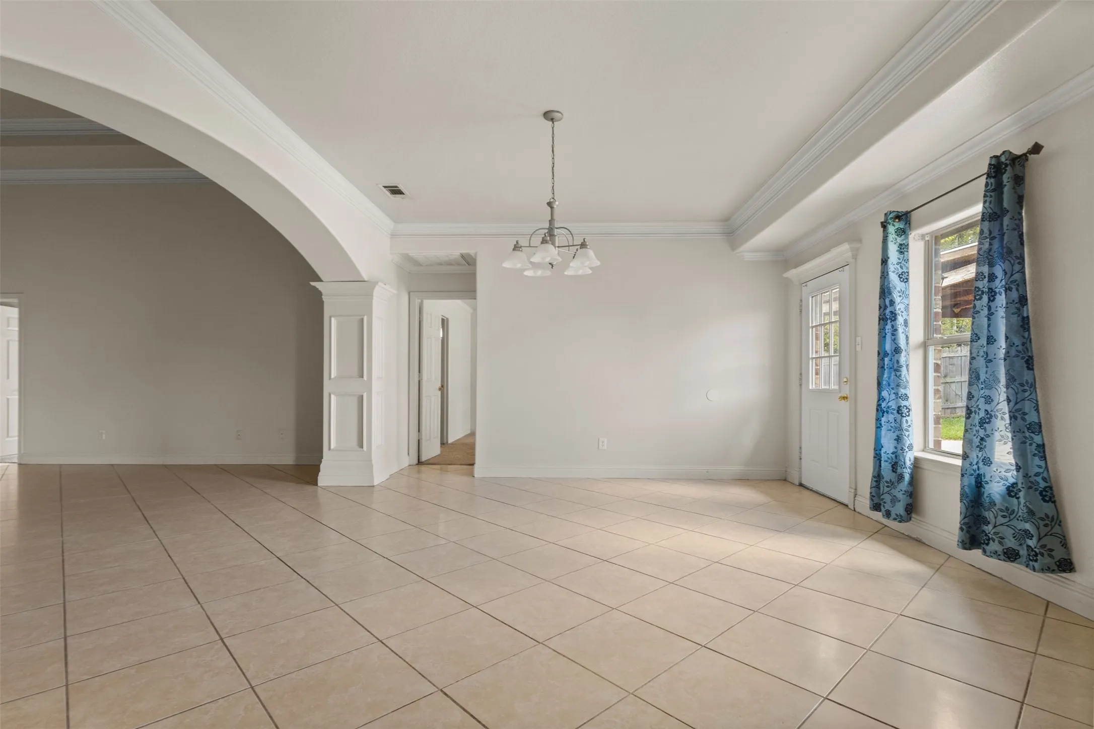 Unfurnished room with light tile patterned flooring, crown molding, arched walkways, and a chandelier