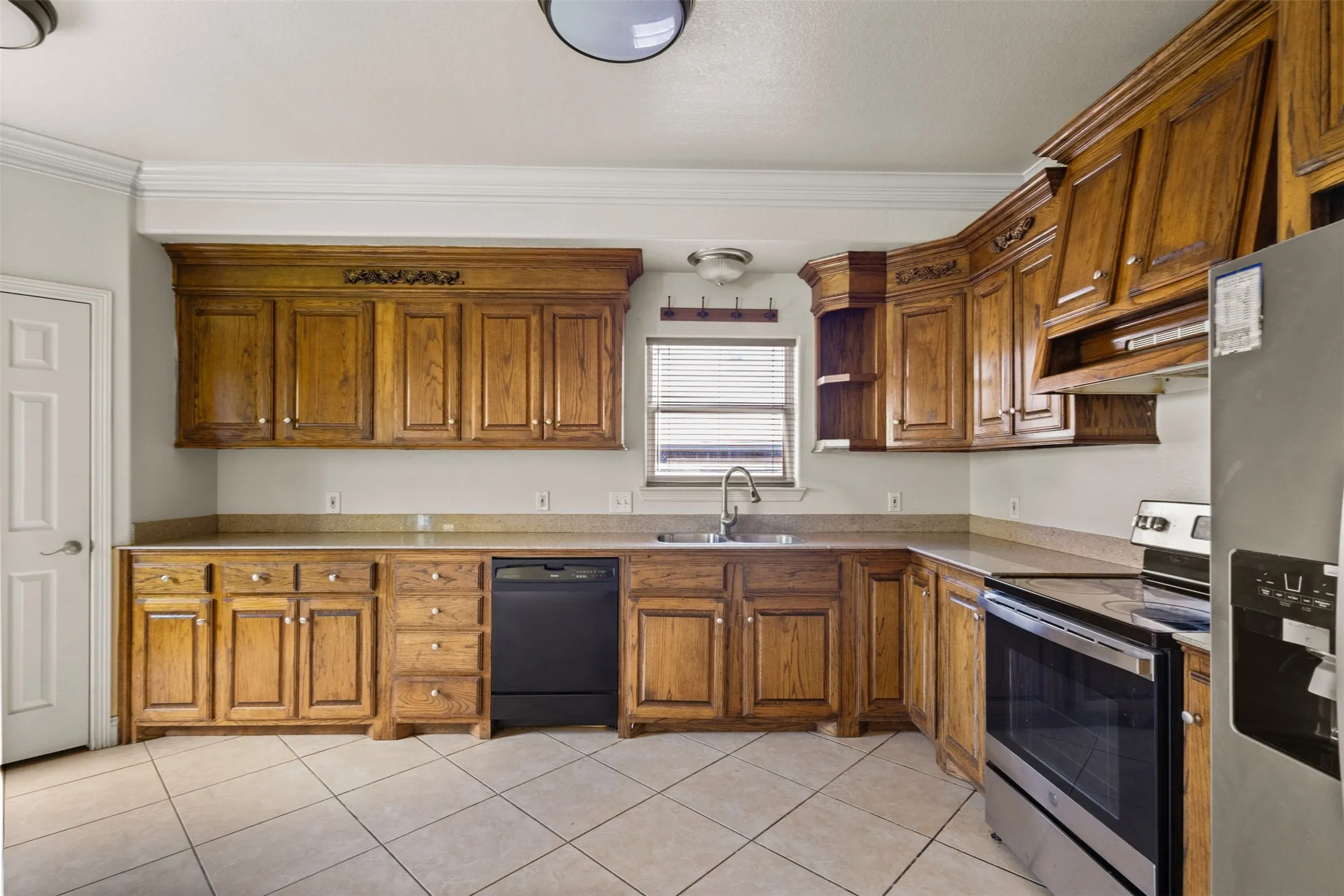 Kitchen with appliances with stainless steel finishes, light tile patterned flooring, brown cabinets, and crown molding