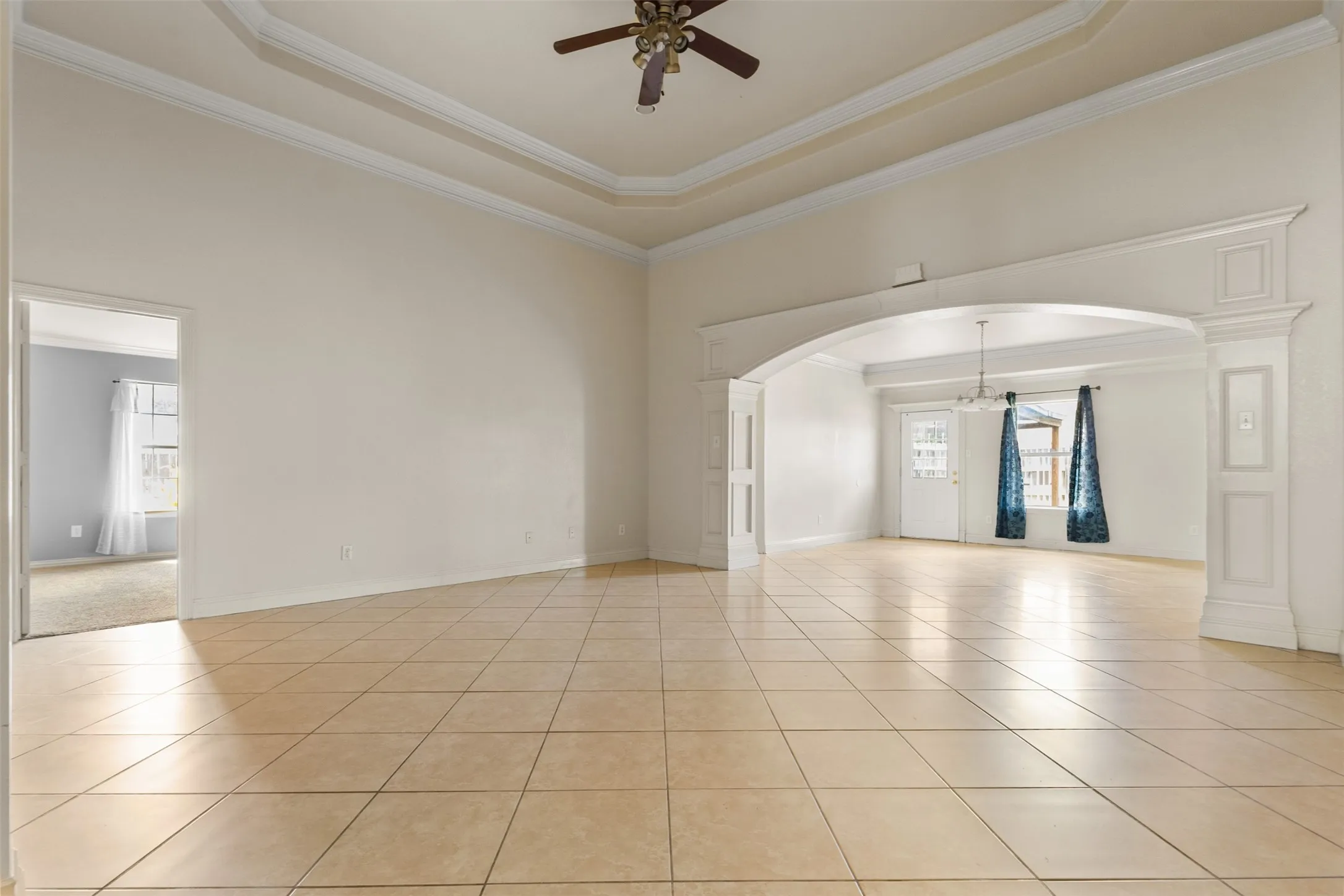 Unfurnished room featuring ornamental molding, a raised ceiling, light tile patterned flooring, arched walkways, and ceiling fan
