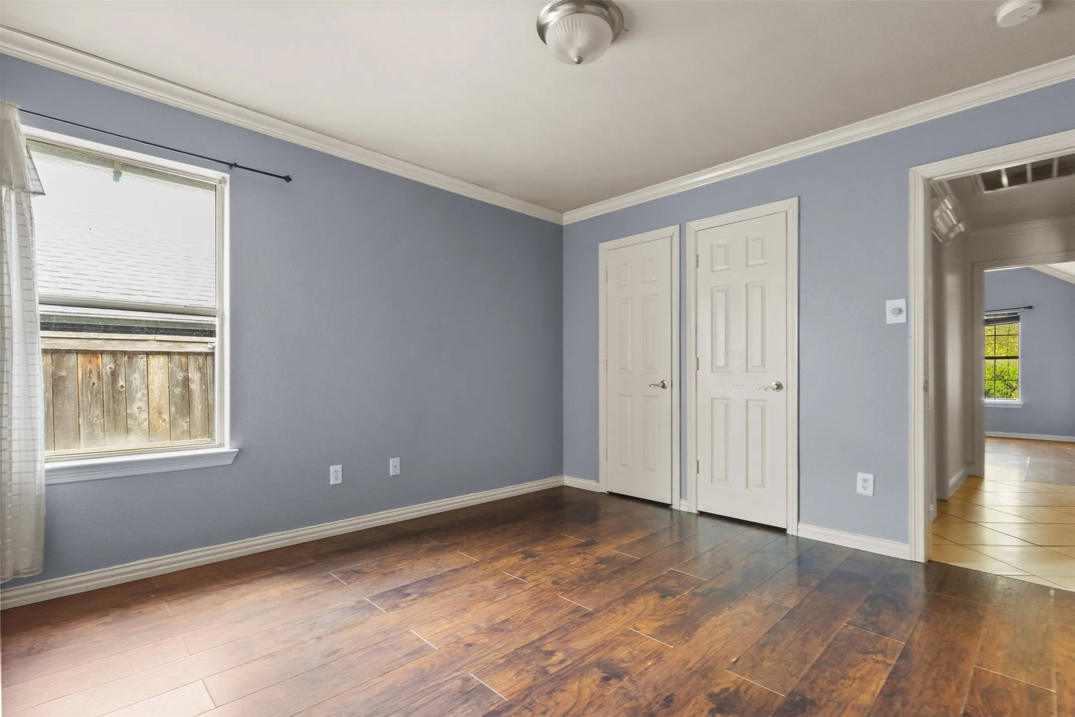 Unfurnished bedroom featuring dark wood finished floors, crown molding, and multiple closets