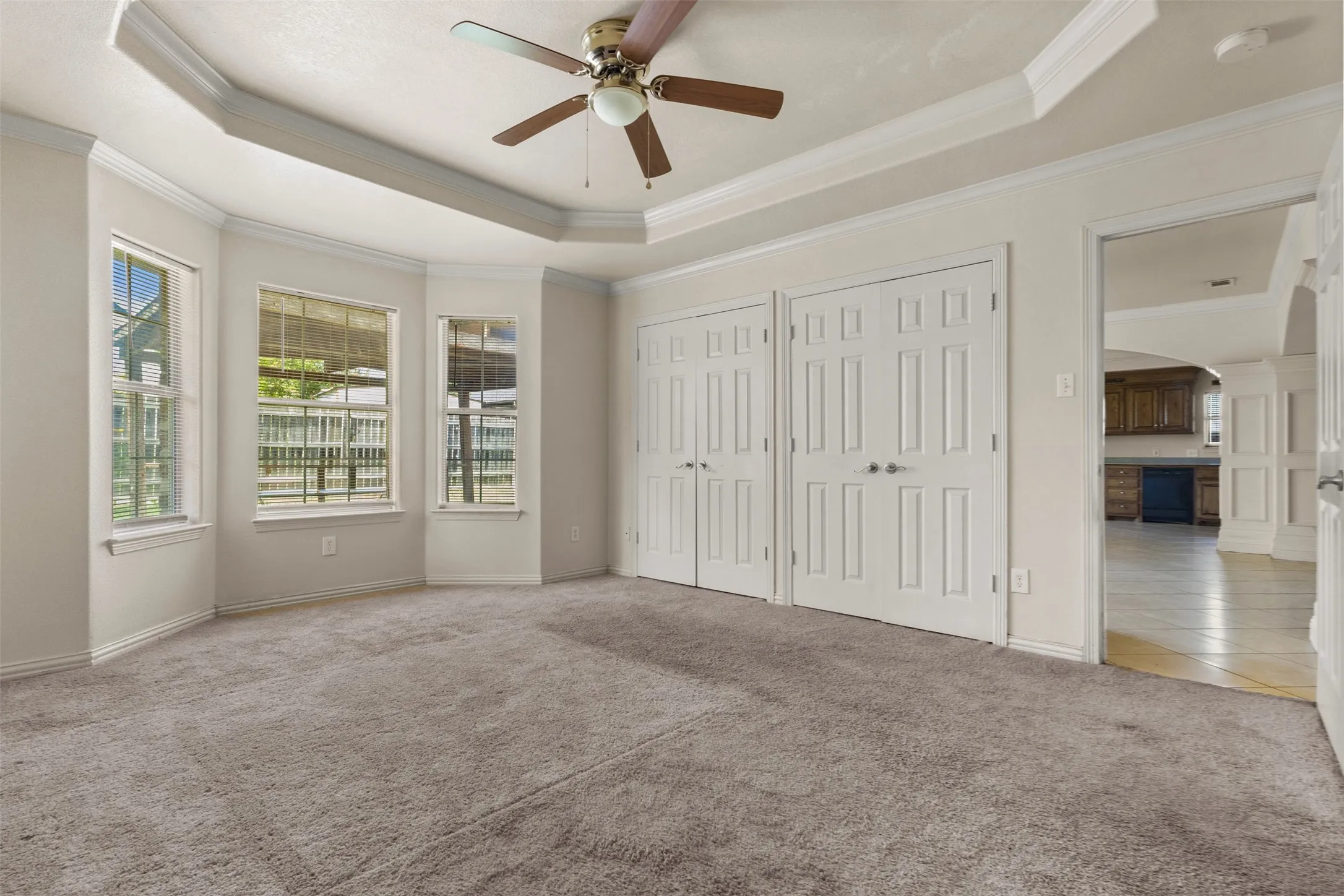 Unfurnished bedroom with a raised ceiling, multiple closets, arched walkways, carpet, and crown molding