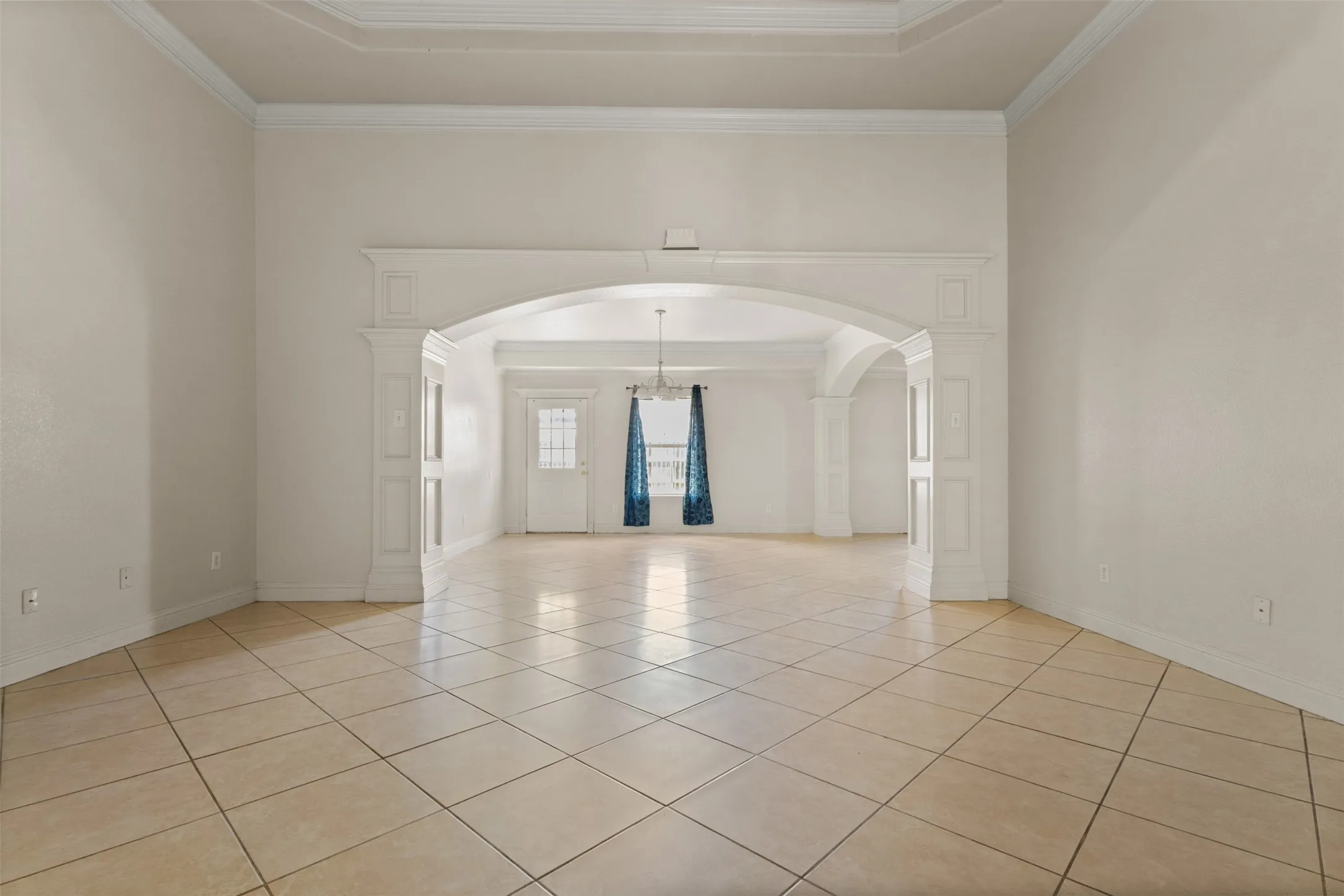 Spare room featuring arched walkways, a tray ceiling, light tile patterned flooring, ornamental molding, and ornate columns