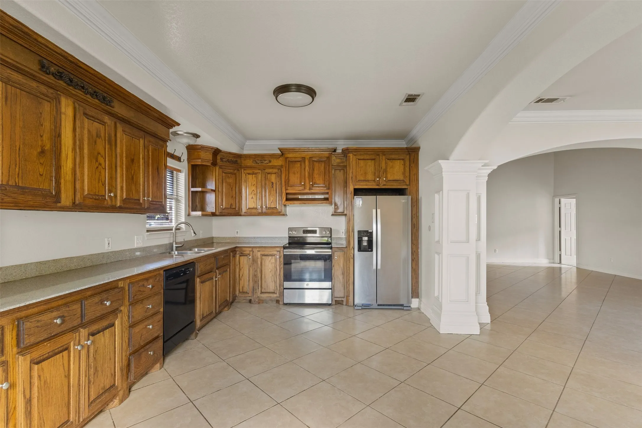 Kitchen featuring crown molding, light tile patterned floors, brown cabinetry, appliances with stainless steel finishes, and arched walkways