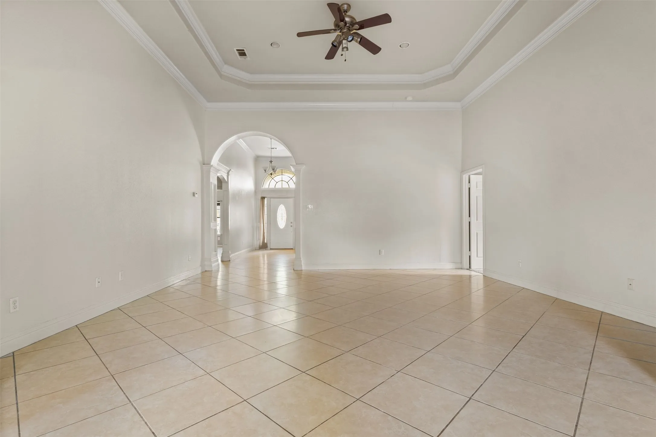 Unfurnished room featuring light tile patterned floors, a raised ceiling, a high ceiling, crown molding, and arched walkways