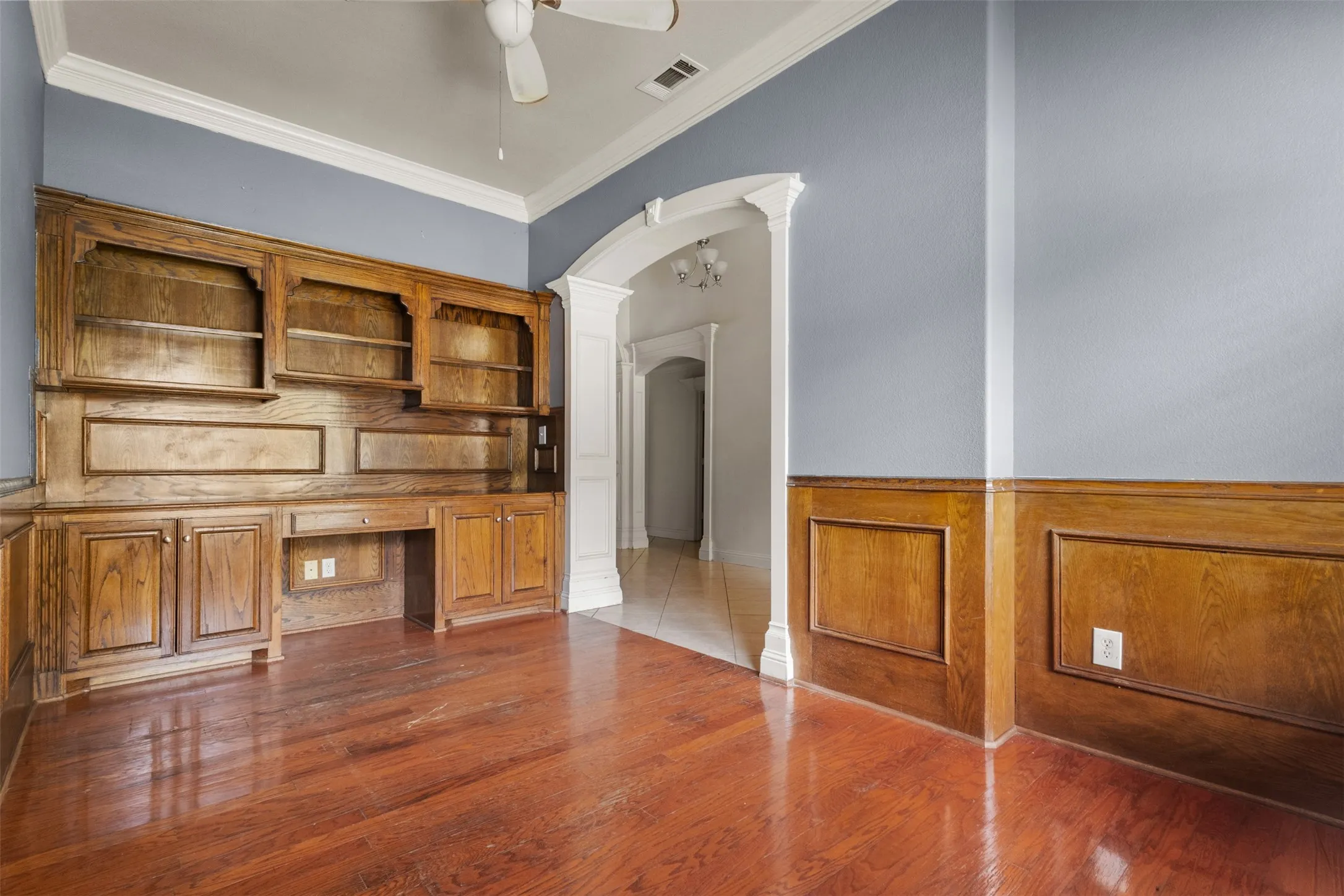 Unfurnished office featuring arched walkways, crown molding, wood finished floors, a ceiling fan, and decorative columns