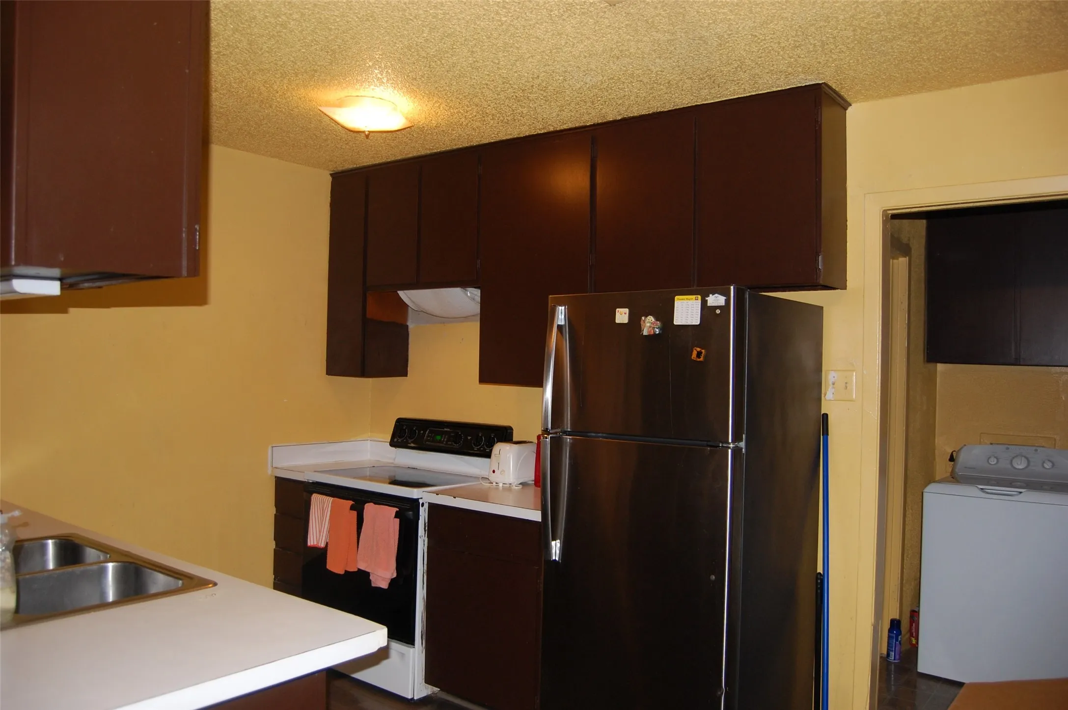 Kitchen featuring freestanding refrigerator, range with electric stovetop, washer / dryer, a textured ceiling, and light countertops