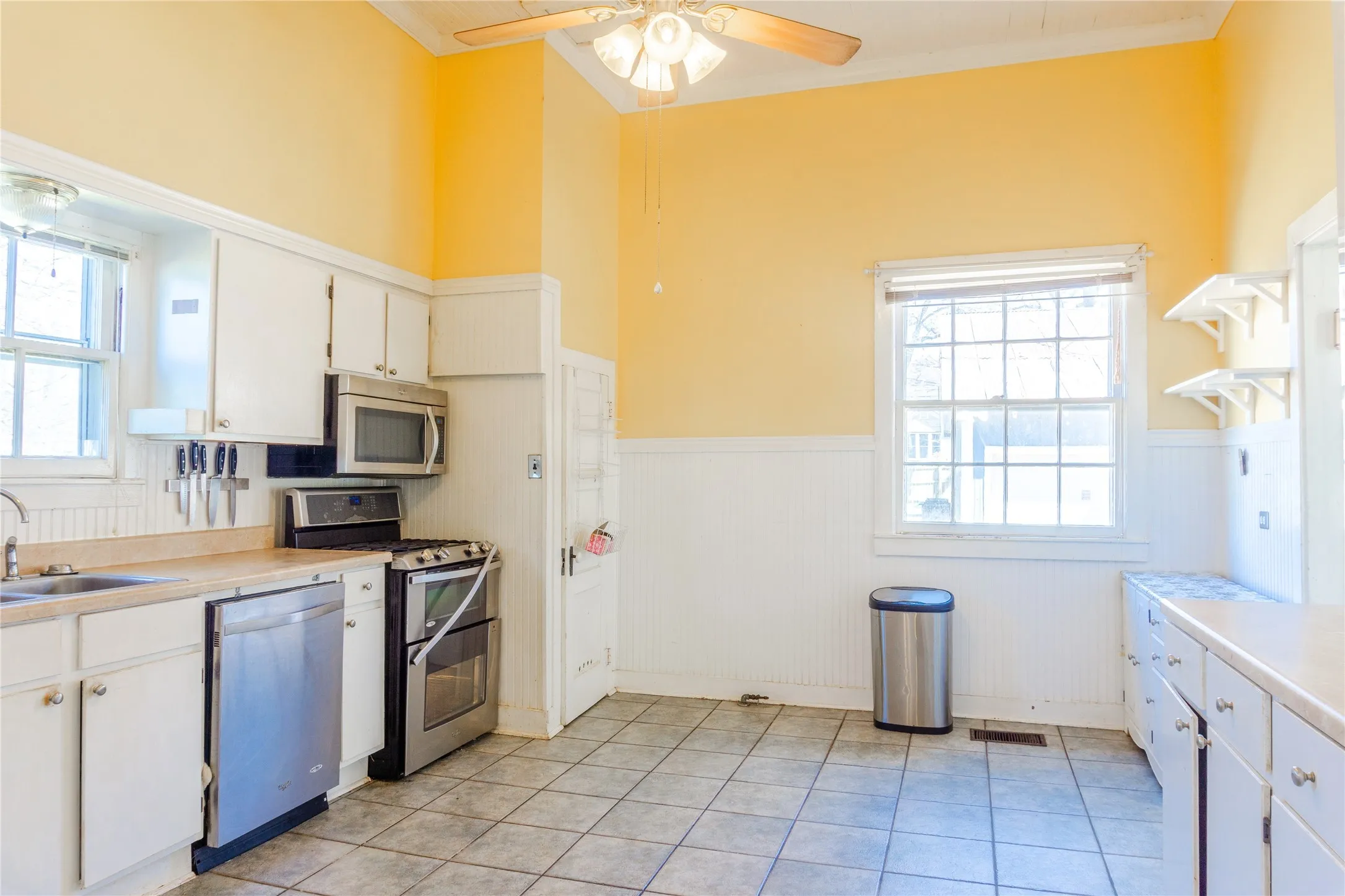 Kitchen with light countertops, white cabinetry, wainscoting, appliances with stainless steel finishes, and plenty of natural light