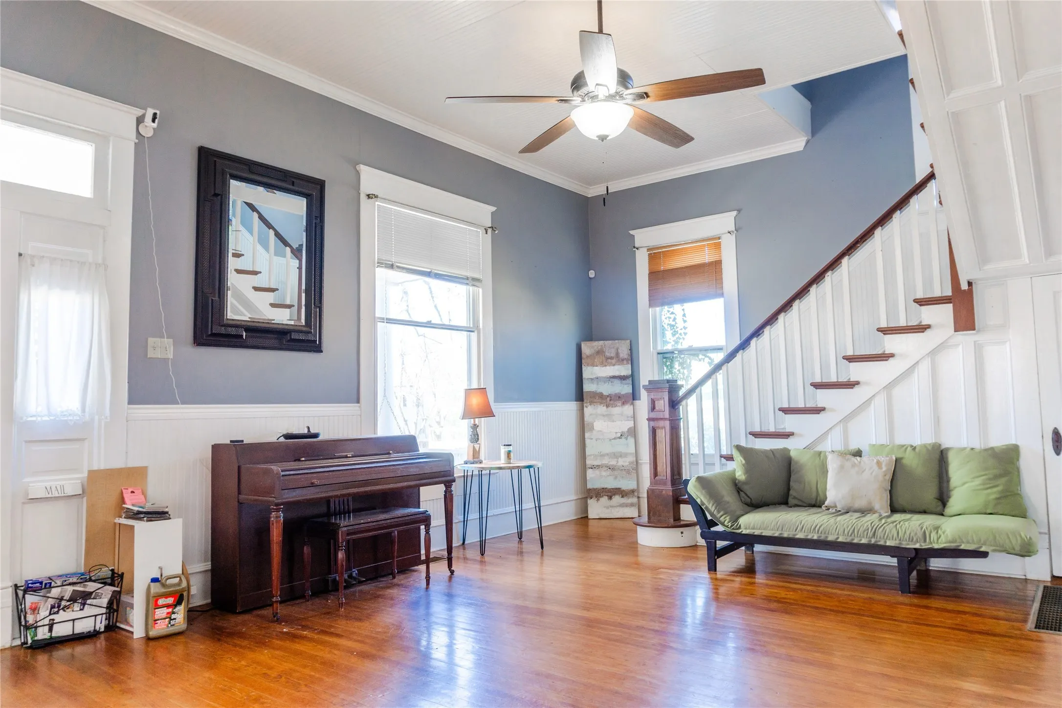 Living area featuring a wainscoted wall, stairway, ornamental molding, wood finished floors, and ceiling fan