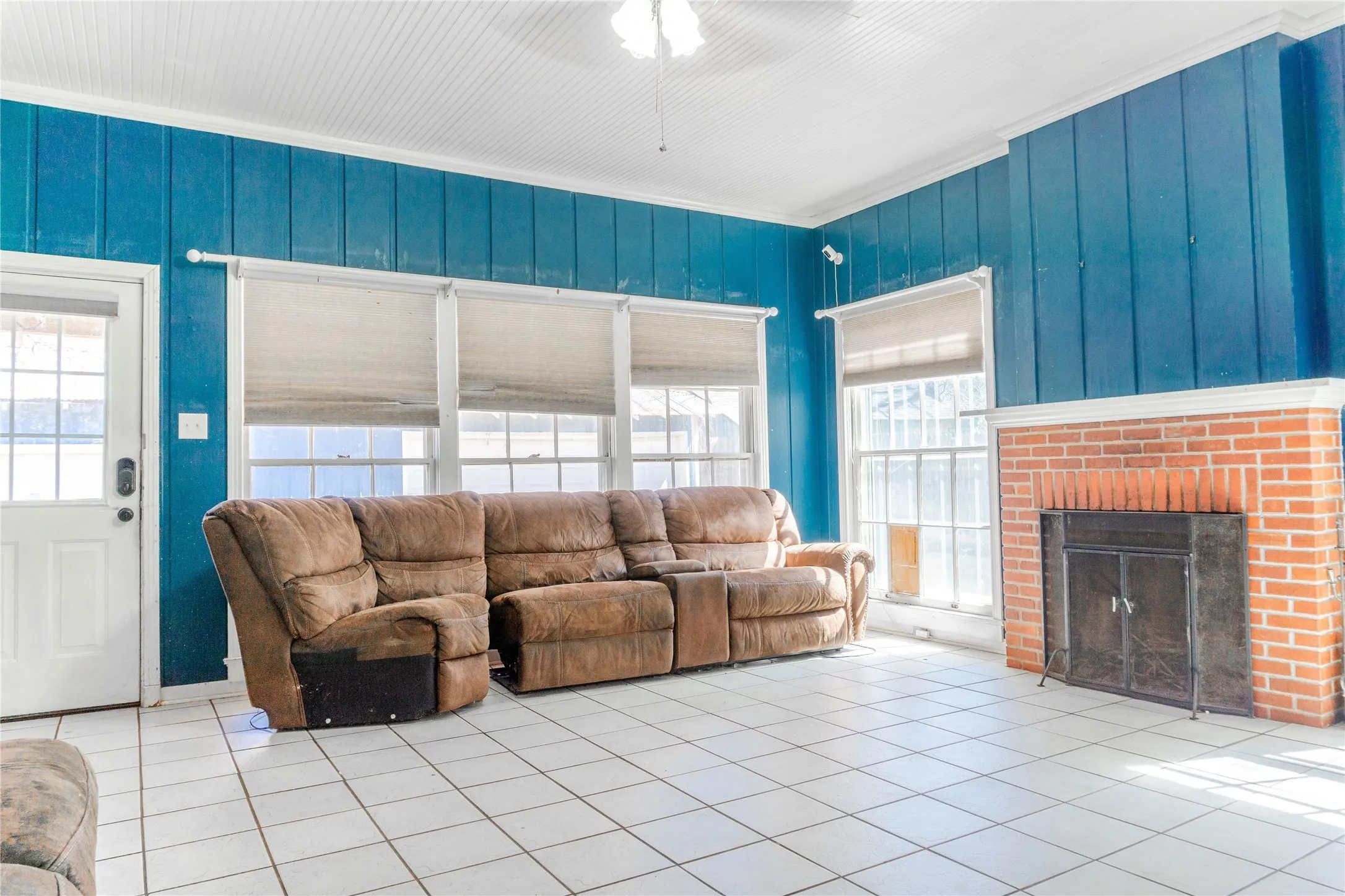 Tiled living area featuring crown molding, a brick fireplace, and ceiling fan