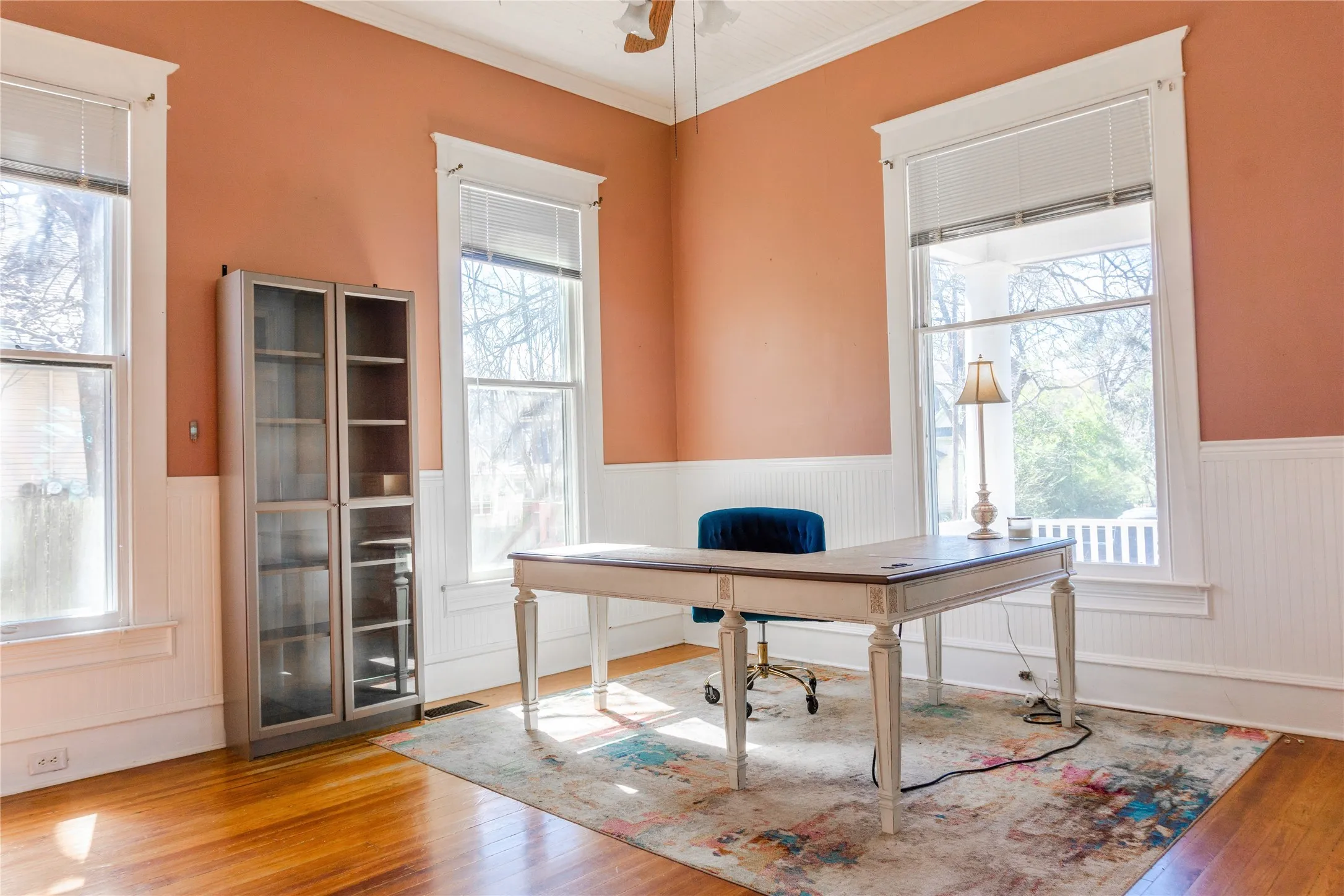 Office space featuring a wainscoted wall, light wood-type flooring, crown molding, and a ceiling fan