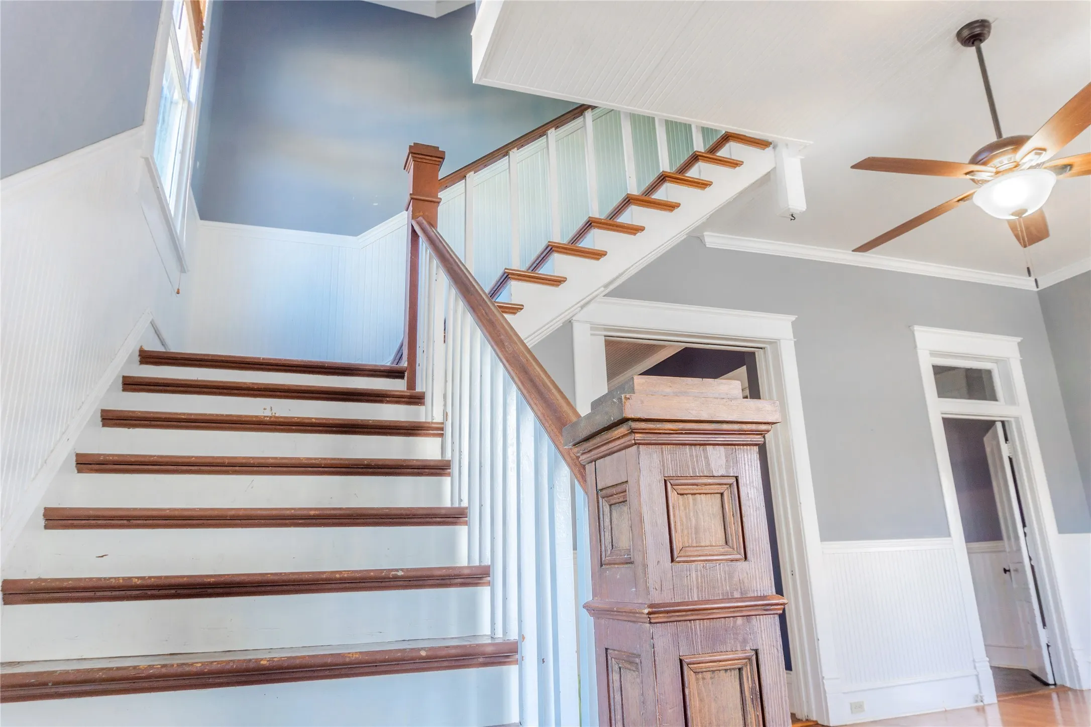 Stairway with wainscoting, a ceiling fan, and crown molding