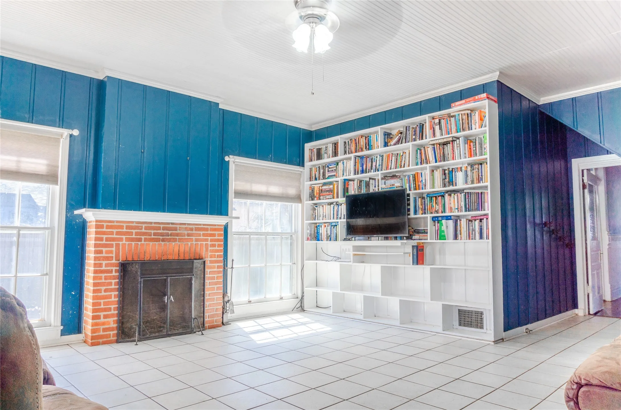 Unfurnished living room featuring tile patterned flooring, crown molding, a fireplace, ceiling fan, and wooden walls