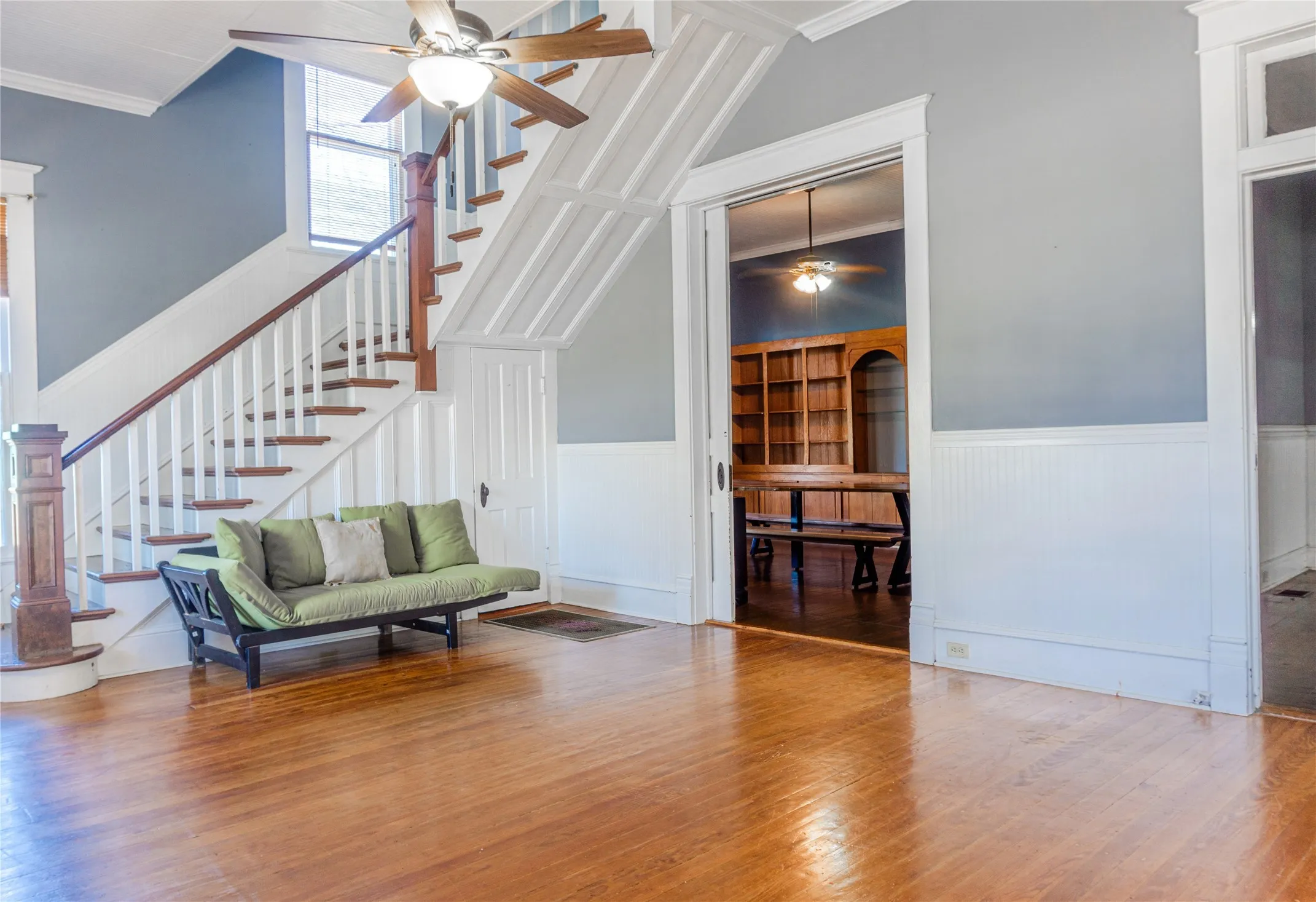 Living area with wainscoting, a ceiling fan, wood finished floors, crown molding, and stairs