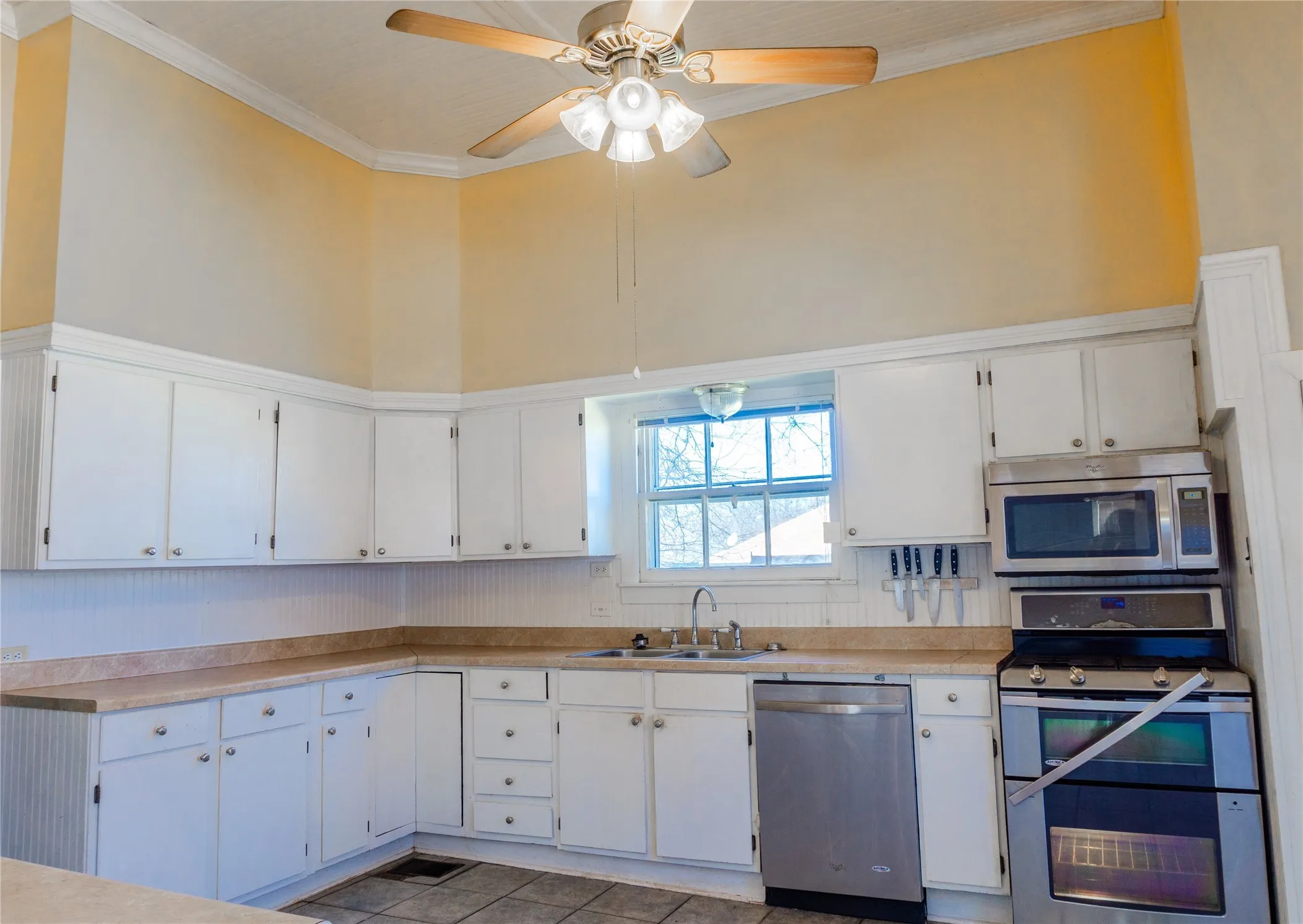 Kitchen with stainless steel appliances, light countertops, white cabinets, ornamental molding, and dark tile patterned floors