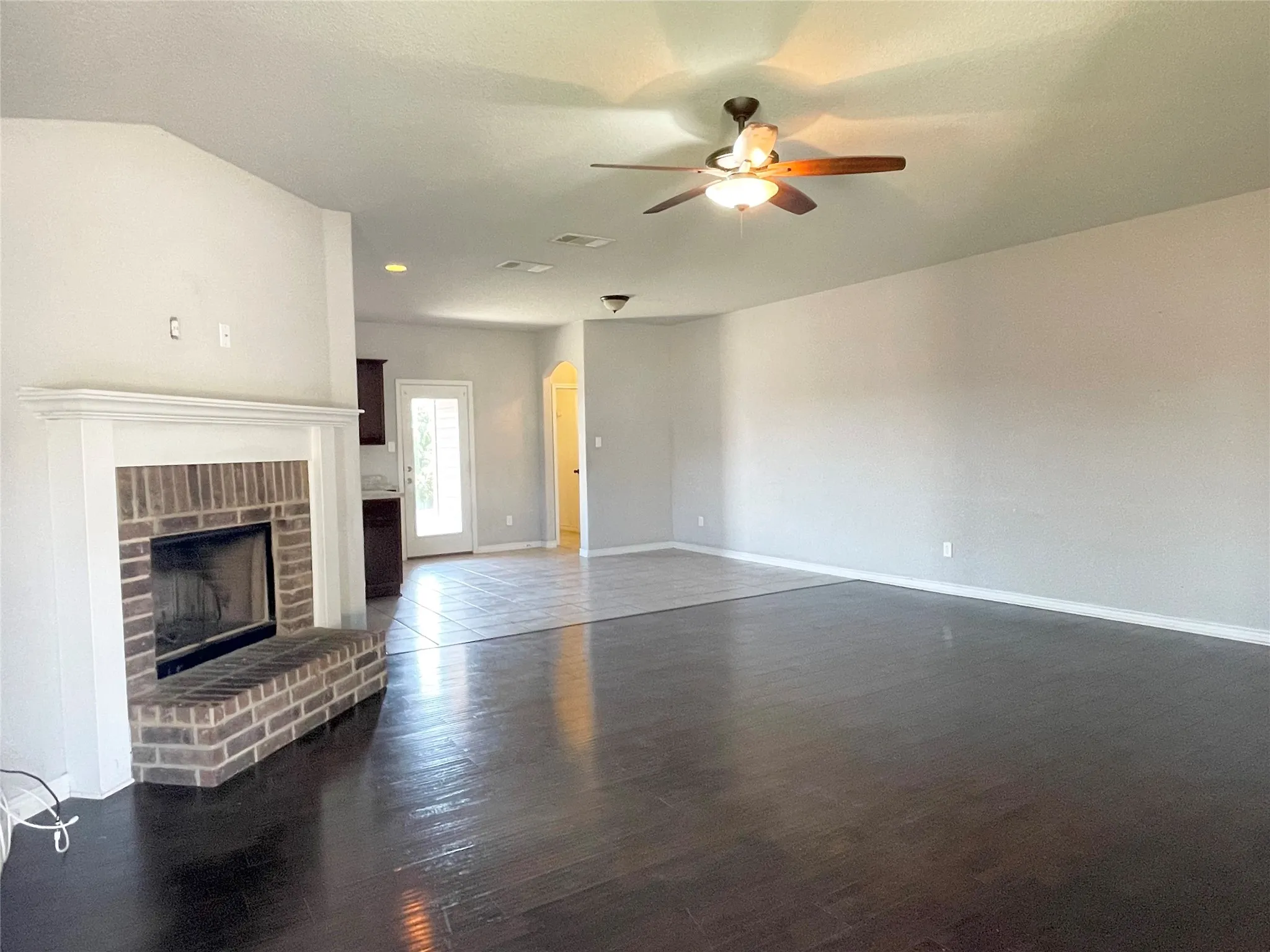 Living room featuring dark wood-style floors, a fireplace, a ceiling fan, and arched walkways