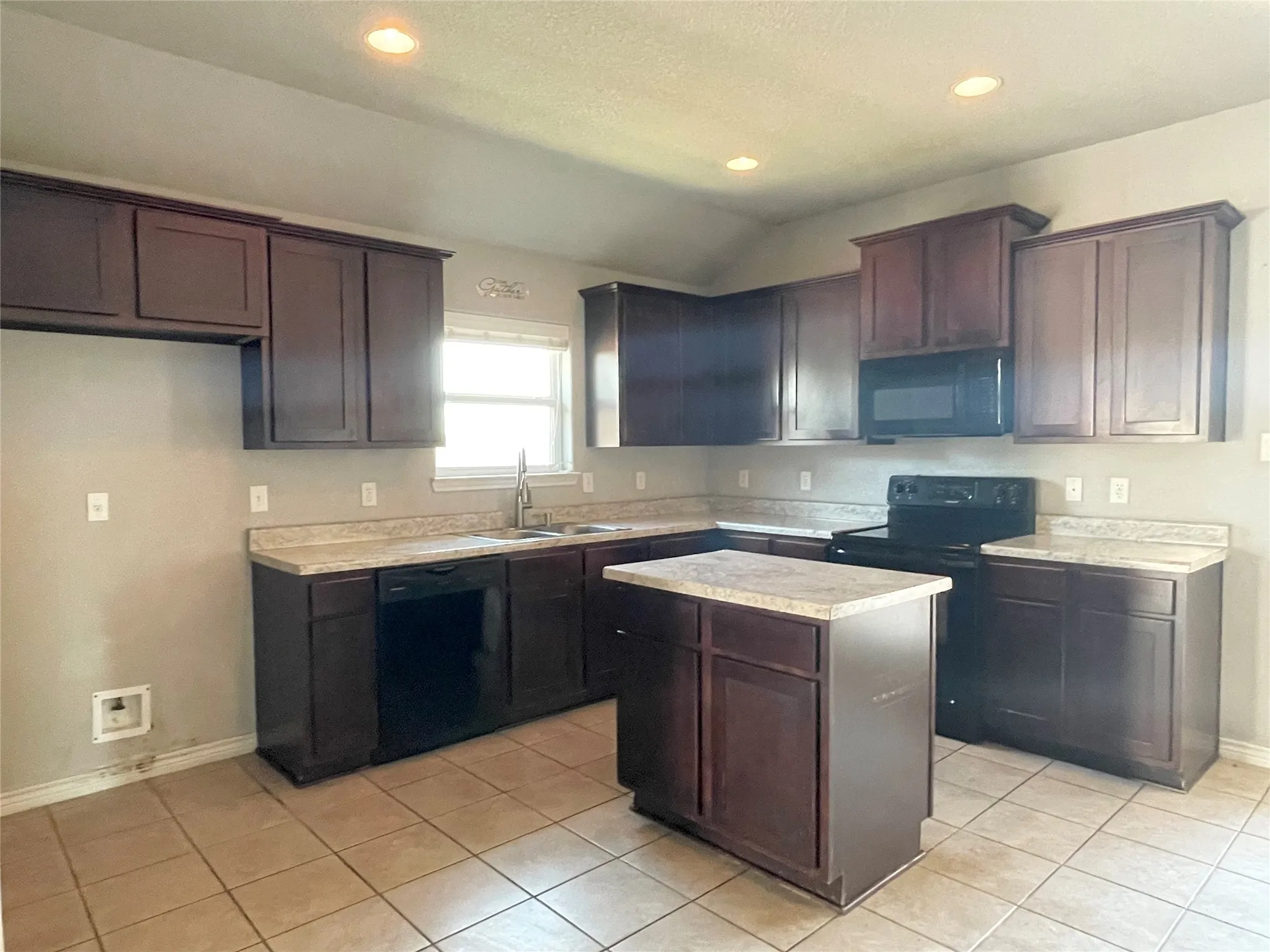 Kitchen with black appliances, light countertops, light tile patterned flooring, a kitchen island, and dark brown cabinetry