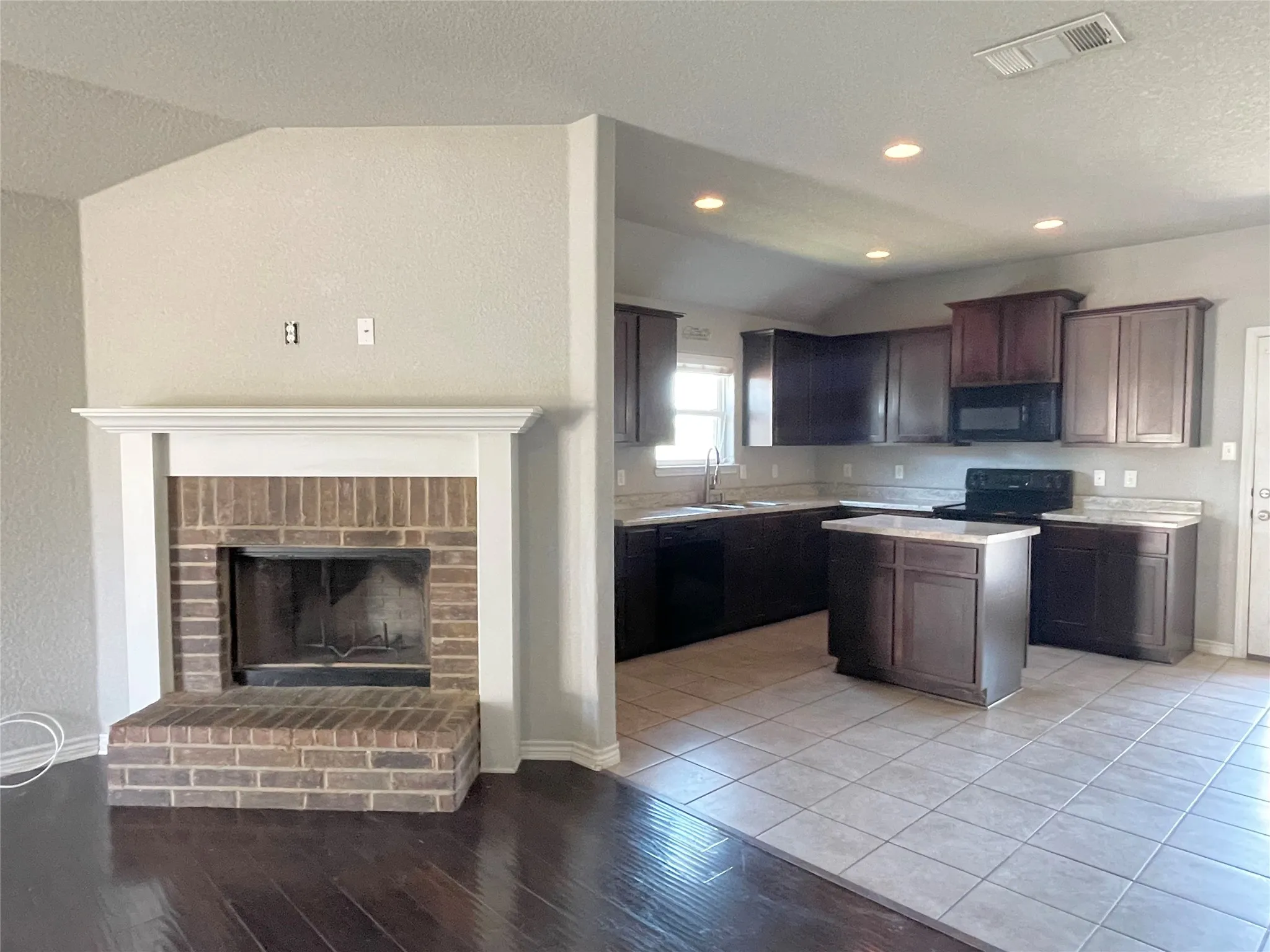 Kitchen with light countertops, a center island, brick fireplace, and black appliances