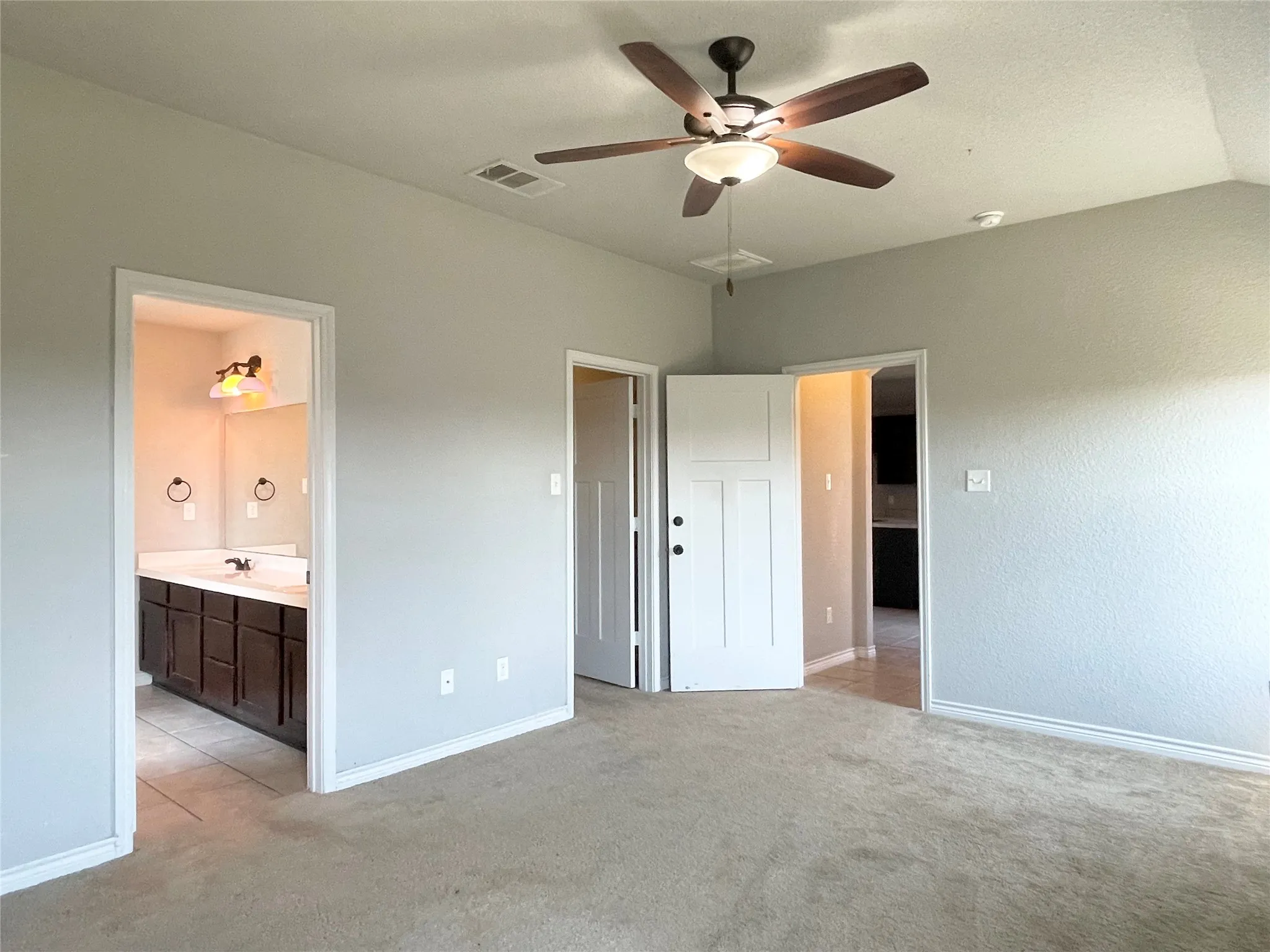 Primary bedroom featuring light carpet, ceiling fan, and ensuite bathroom