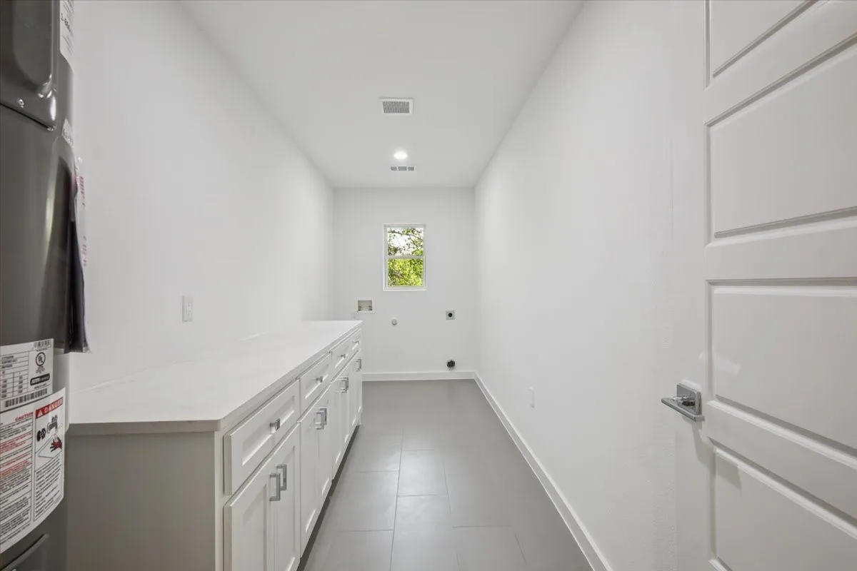 Washroom with hookup for an electric dryer, water heater, hookup for a washing machine, dark tile patterned floors, and cabinet space