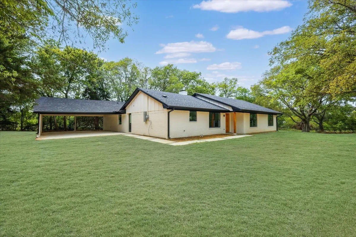 Rear view of property with a yard, brick siding, a chimney, and roof with shingles