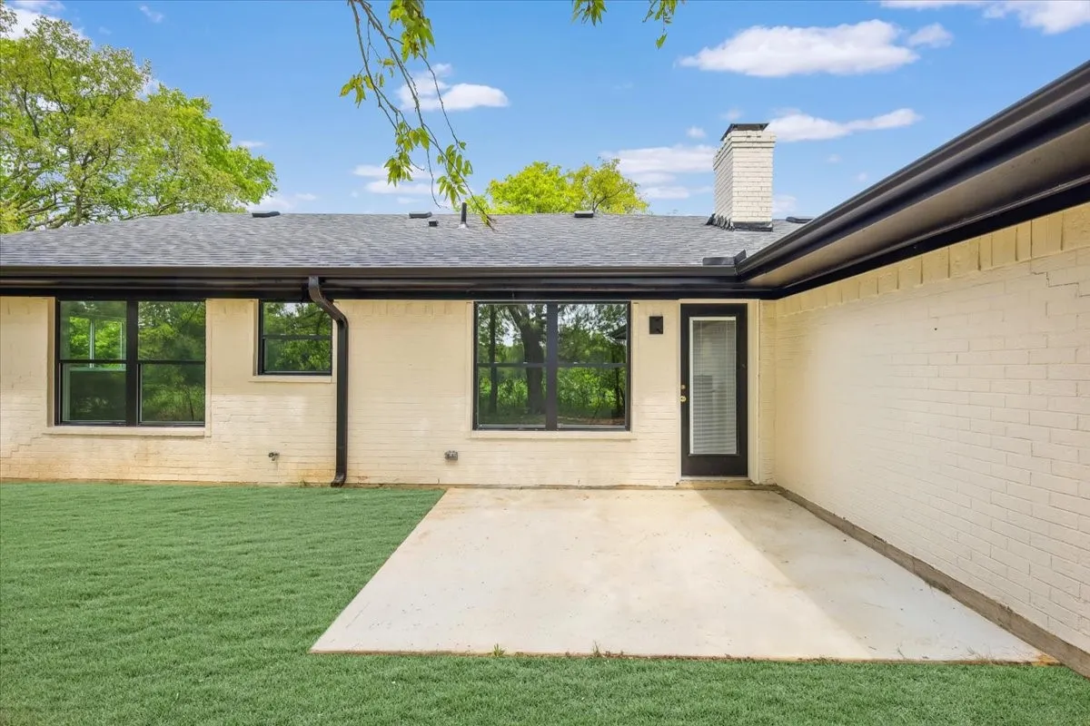 Rear view of property with a shingled roof, brick siding, a yard, a patio, and a chimney