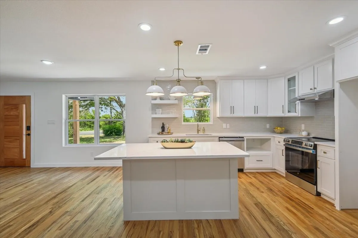Kitchen featuring stainless steel appliances, hanging light fixtures, backsplash, white cabinets, and a center island