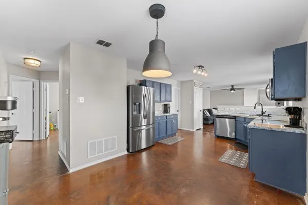 Kitchen featuring blue cabinets, stainless steel appliances, hanging light fixtures, a ceiling fan, and light stone countertops