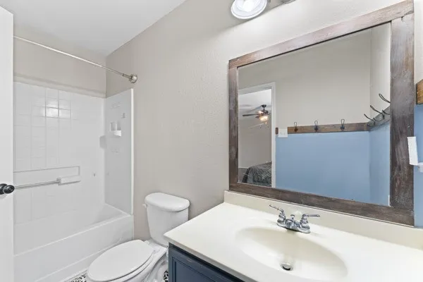 Ensuite bathroom with vanity, washtub / shower combination, a textured wall, and ceiling fan