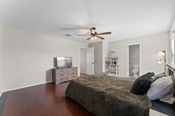 Bedroom with finished concrete floors, ensuite bathroom, and a ceiling fan