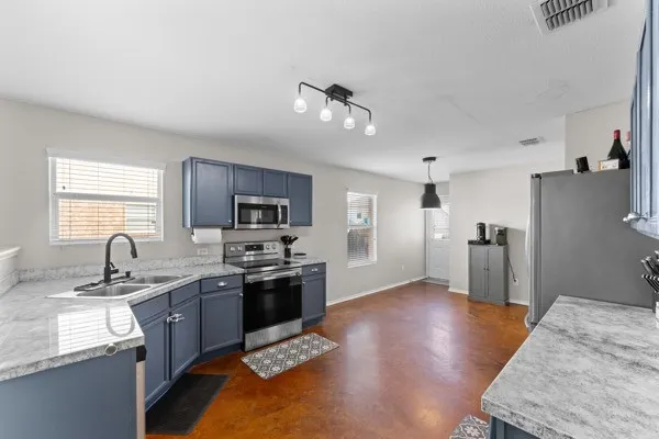 Kitchen with light countertops, appliances with stainless steel finishes, pendant lighting, and healthy amount of natural light