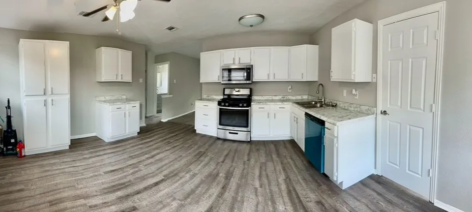 Kitchen featuring ceiling fan, white cabinets, stainless steel appliances, sink, and vinyl plank flooring