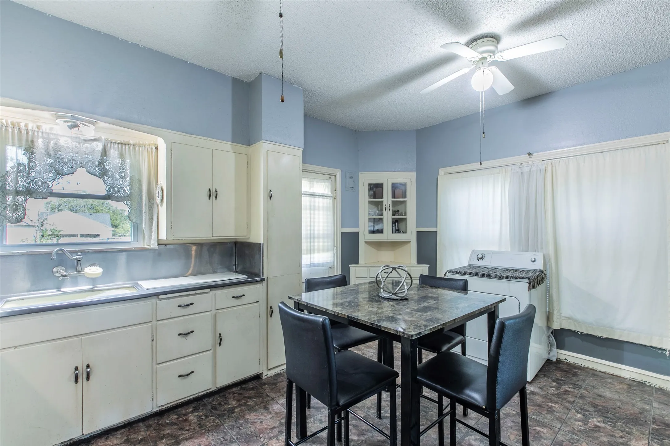 Kitchen with a textured ceiling, stone finish flooring, a ceiling fan, and white cabinets