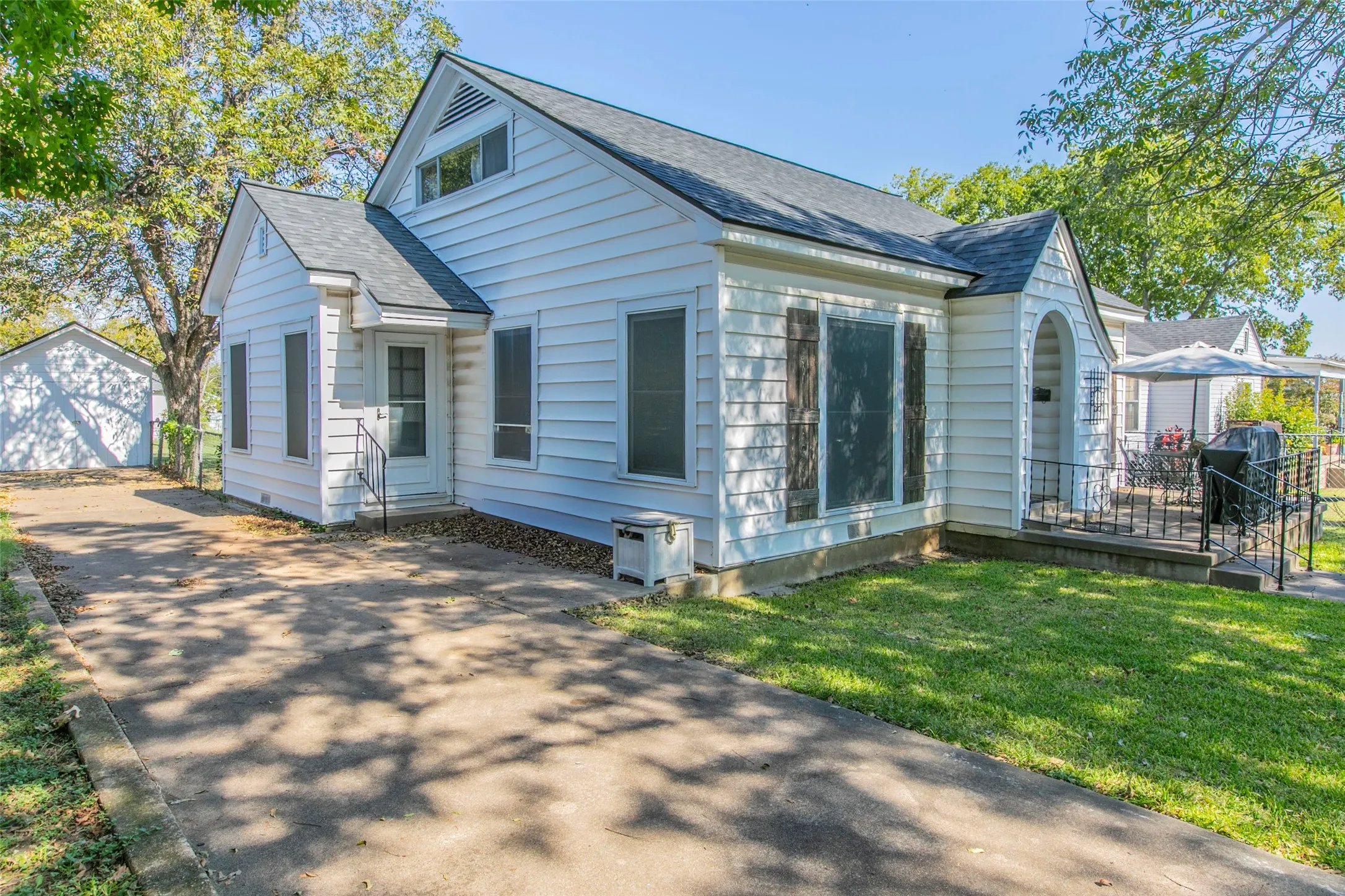 View of front of house featuring roof with shingles, an outdoor structure, a detached garage, driveway, and a front lawn