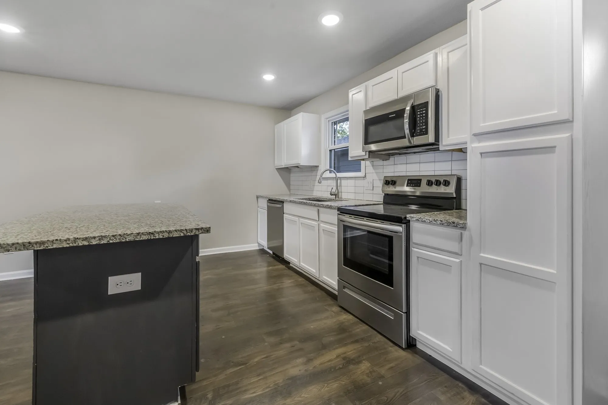Kitchen featuring appliances with stainless steel finishes, tasteful backsplash, dark wood-style floors, light stone countertops, and recessed lighting