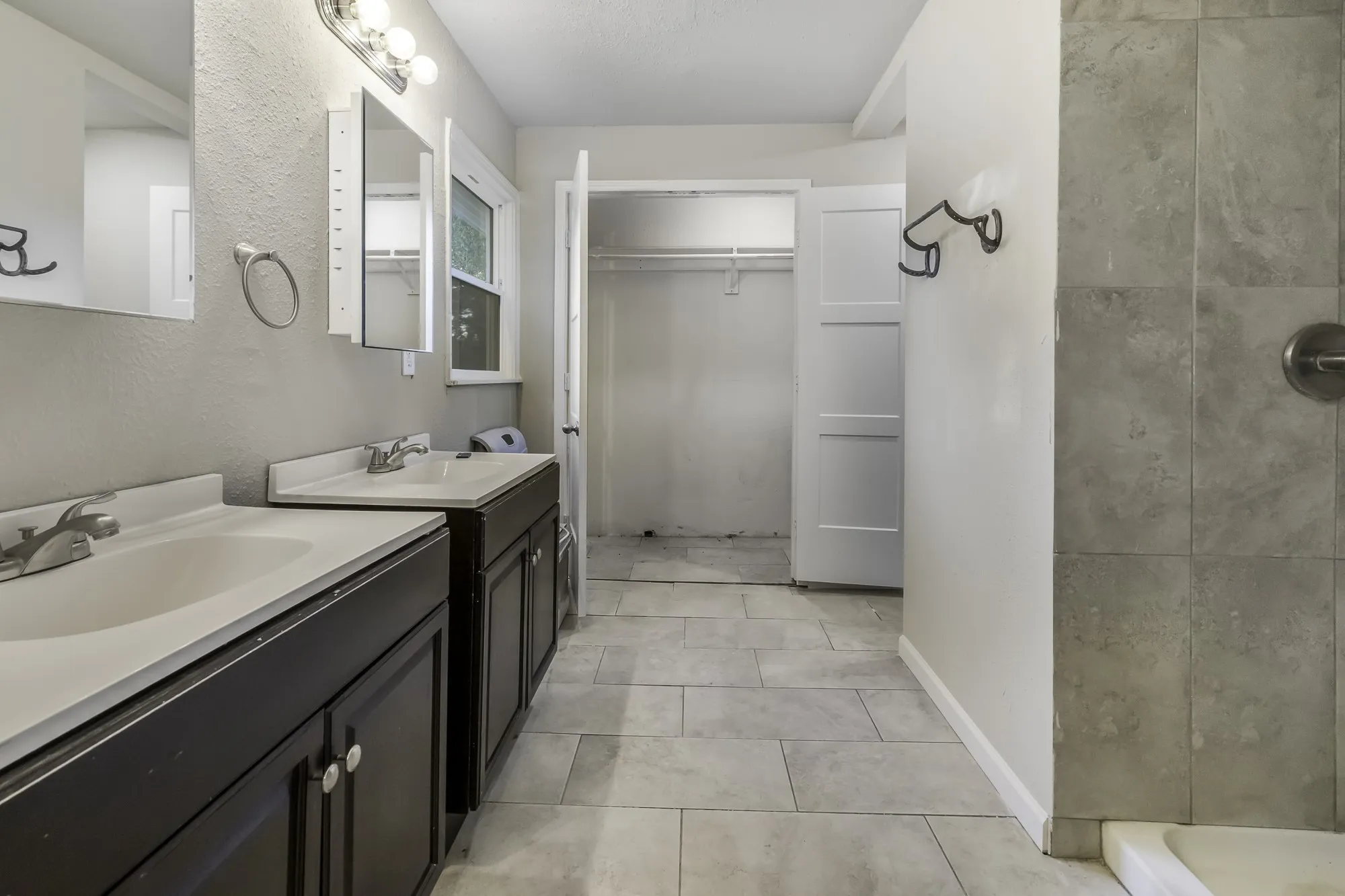 Bathroom with two vanities, a walk in closet, a textured wall, a shower stall, and light tile patterned flooring