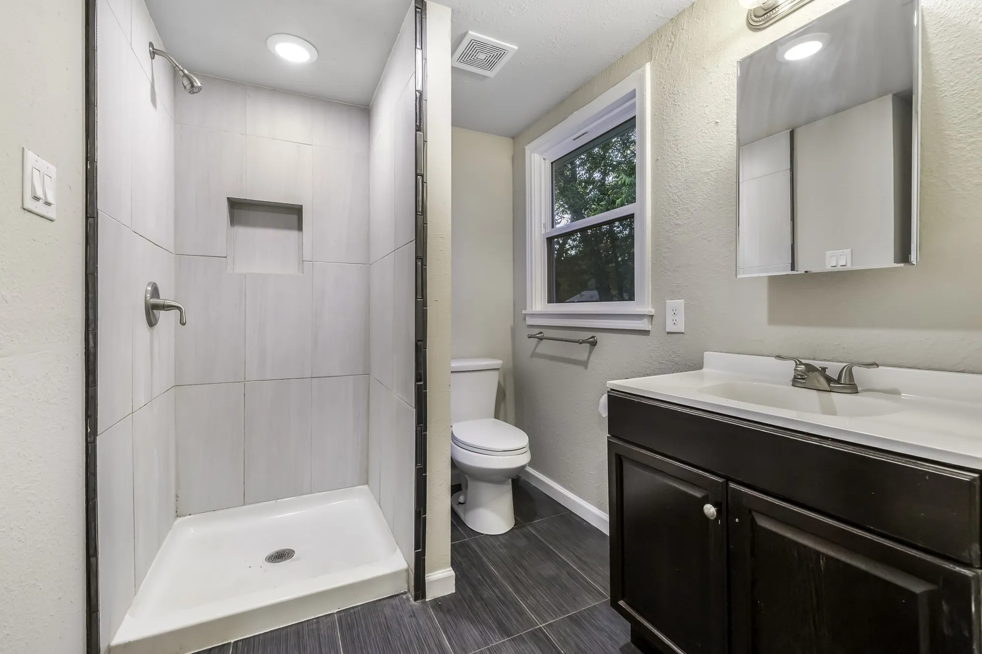 Bathroom featuring vanity, a textured wall, a stall shower, and dark tile patterned flooring