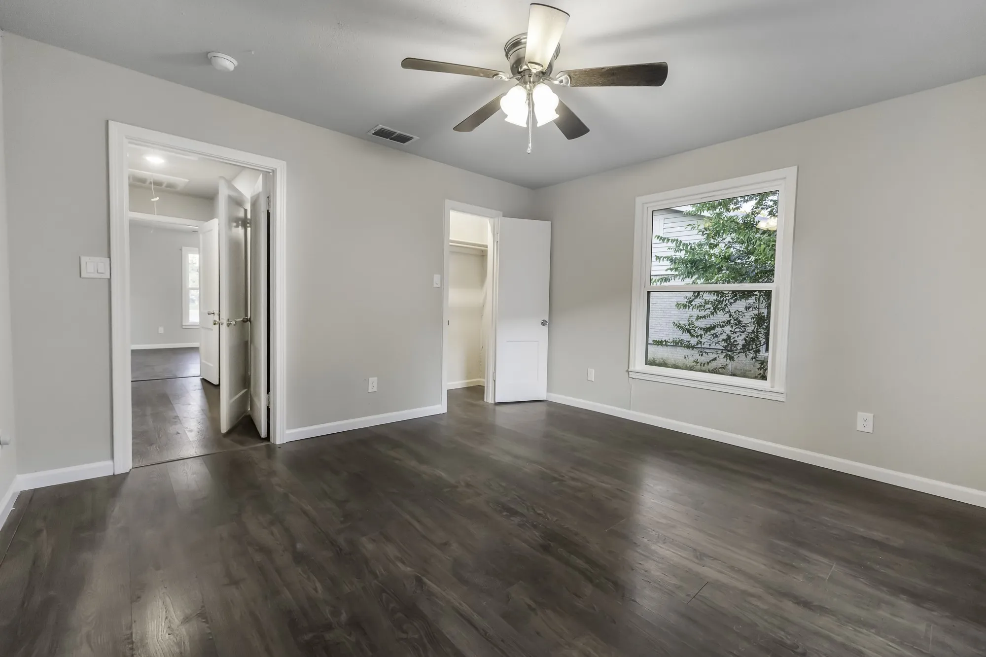 Unfurnished bedroom with a spacious closet, dark wood-style flooring, and a ceiling fan