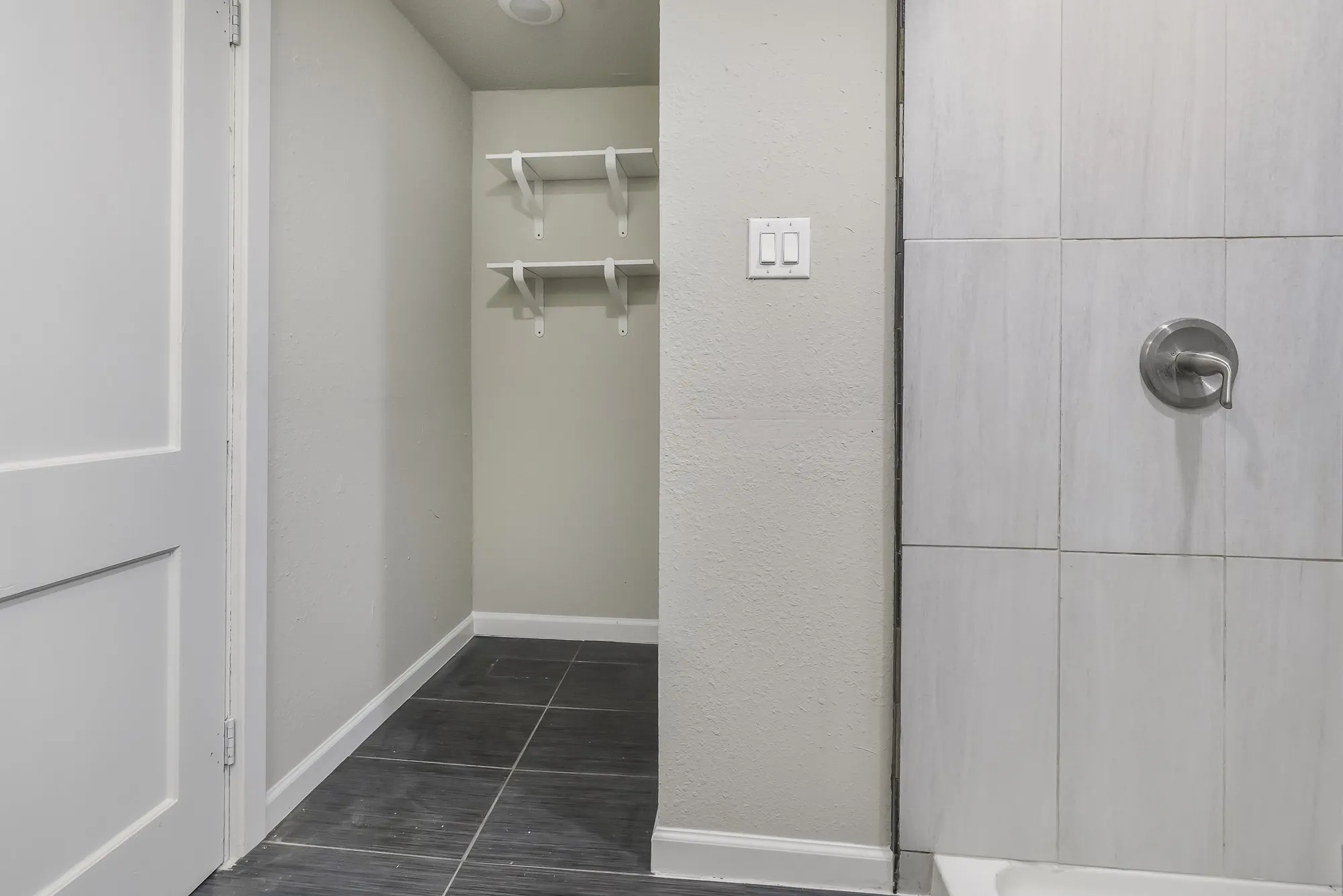 Bathroom featuring a shower, dark tile patterned floors, and a textured wall