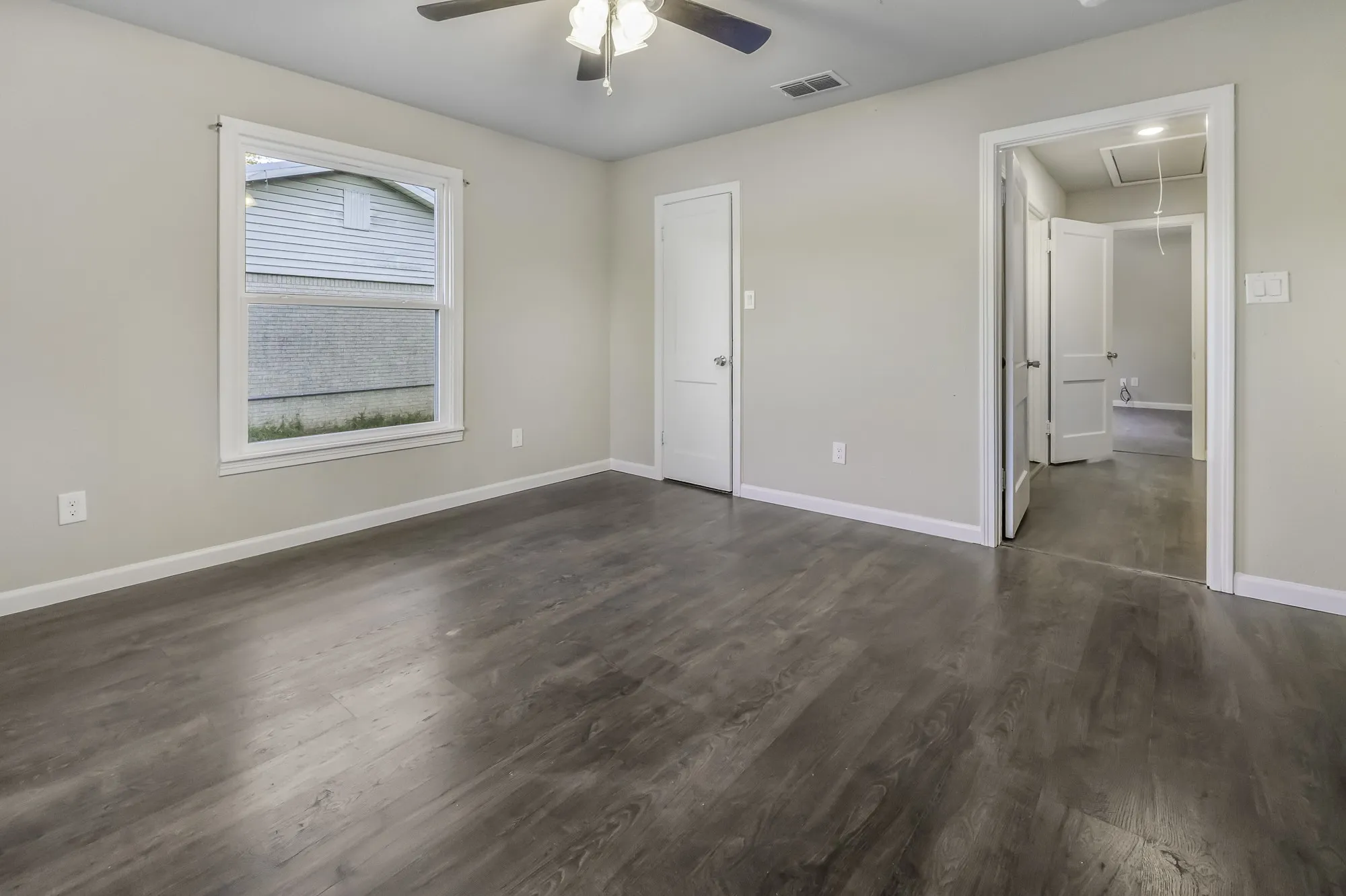 Unfurnished bedroom featuring attic access, dark wood-style flooring, and a ceiling fan