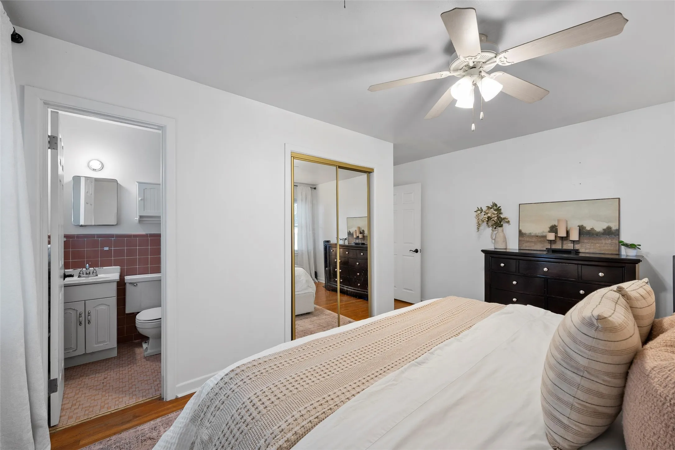 Bedroom featuring wood finished floors, tile walls, a closet, a ceiling fan, and ensuite bathroom