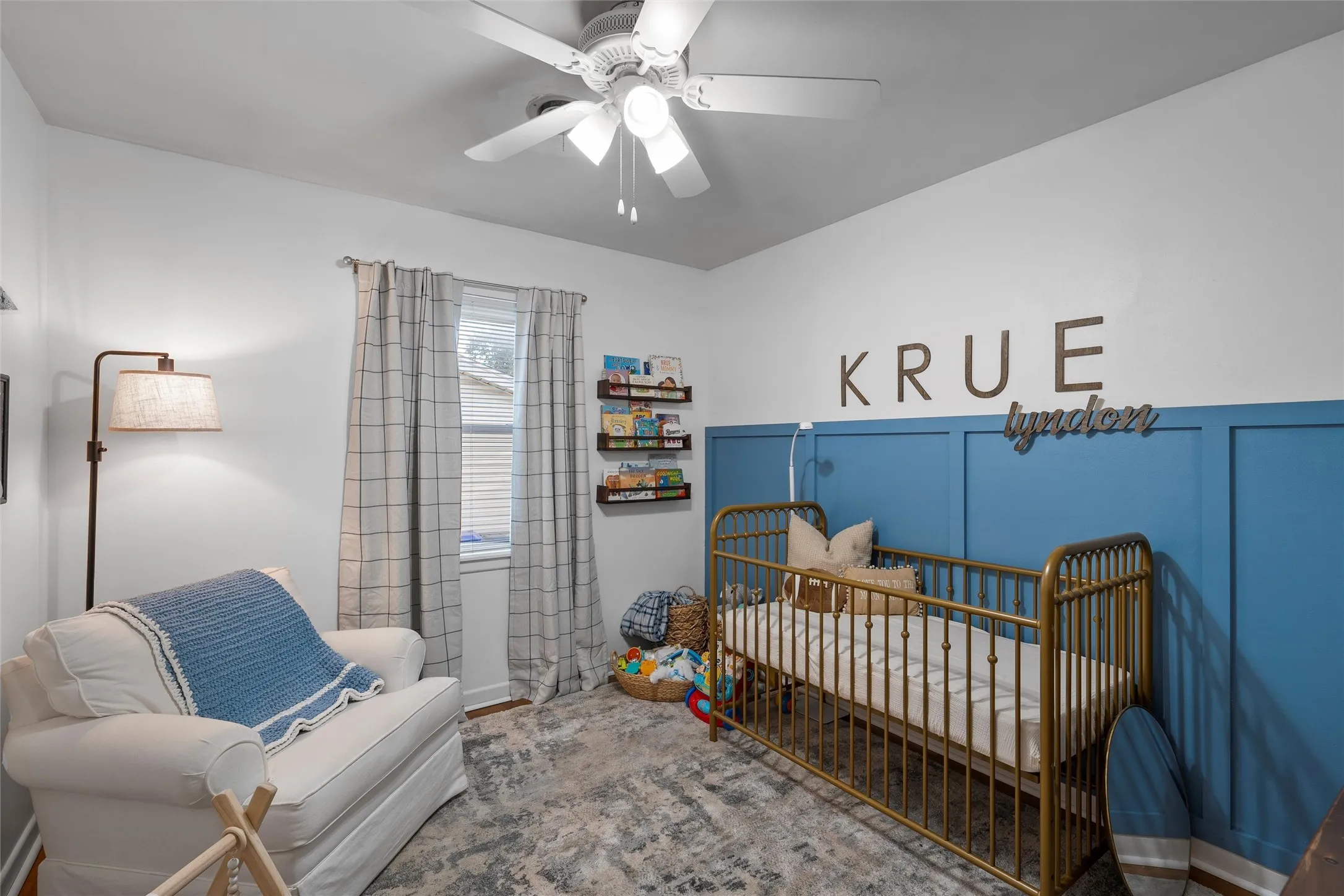 Bedroom featuring a crib, a ceiling fan, wood finished floors, and a decorative wall