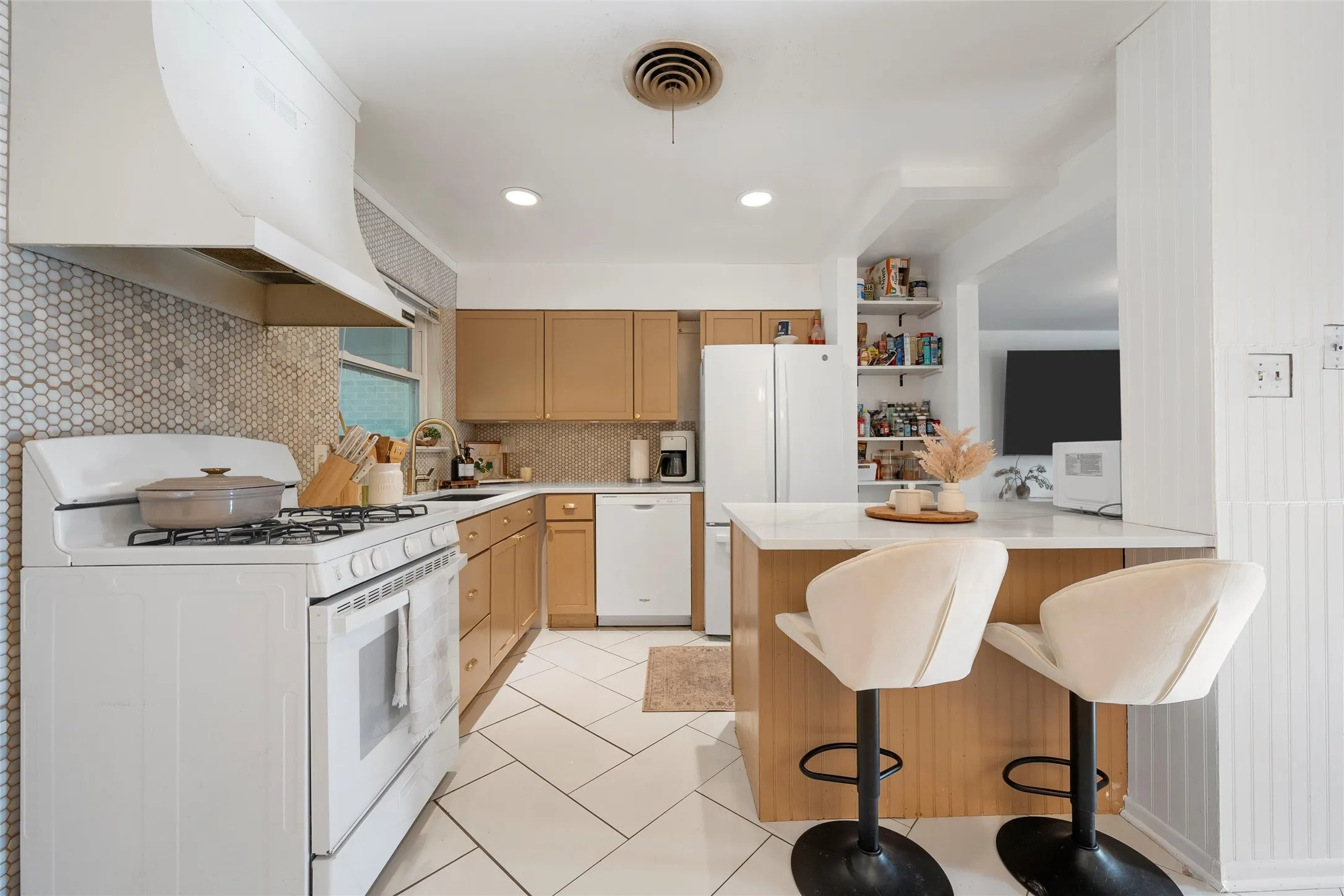 Kitchen featuring white appliances, tasteful backsplash, range hood, a kitchen bar, and light tile patterned floors