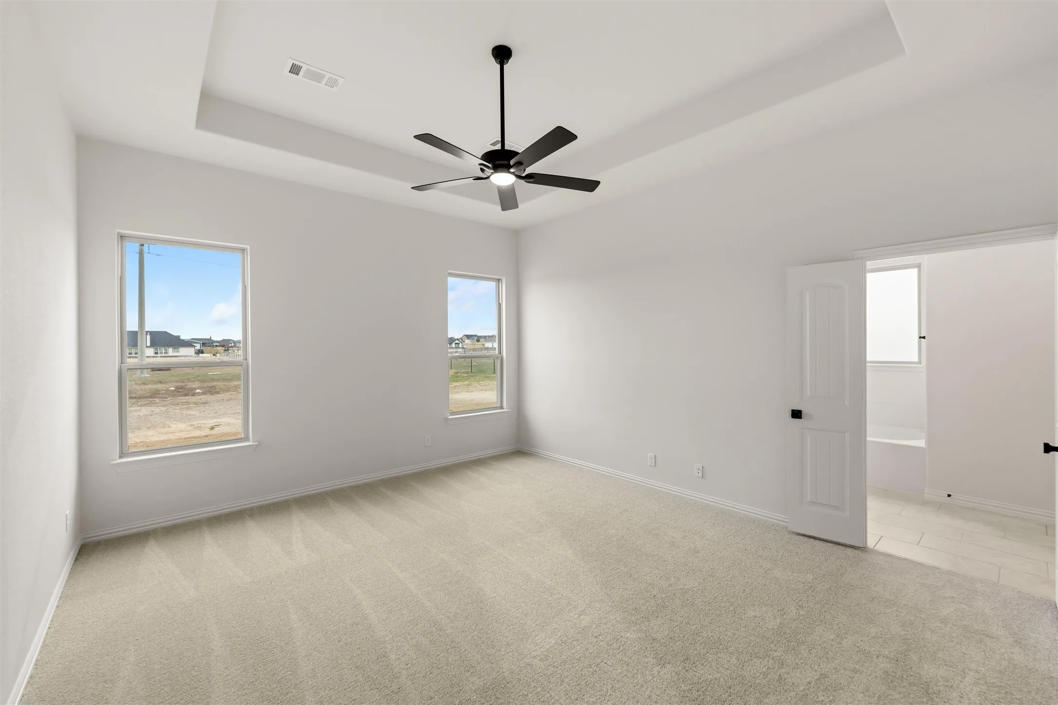 Unfurnished room with light colored carpet, a ceiling fan, and a tray ceiling