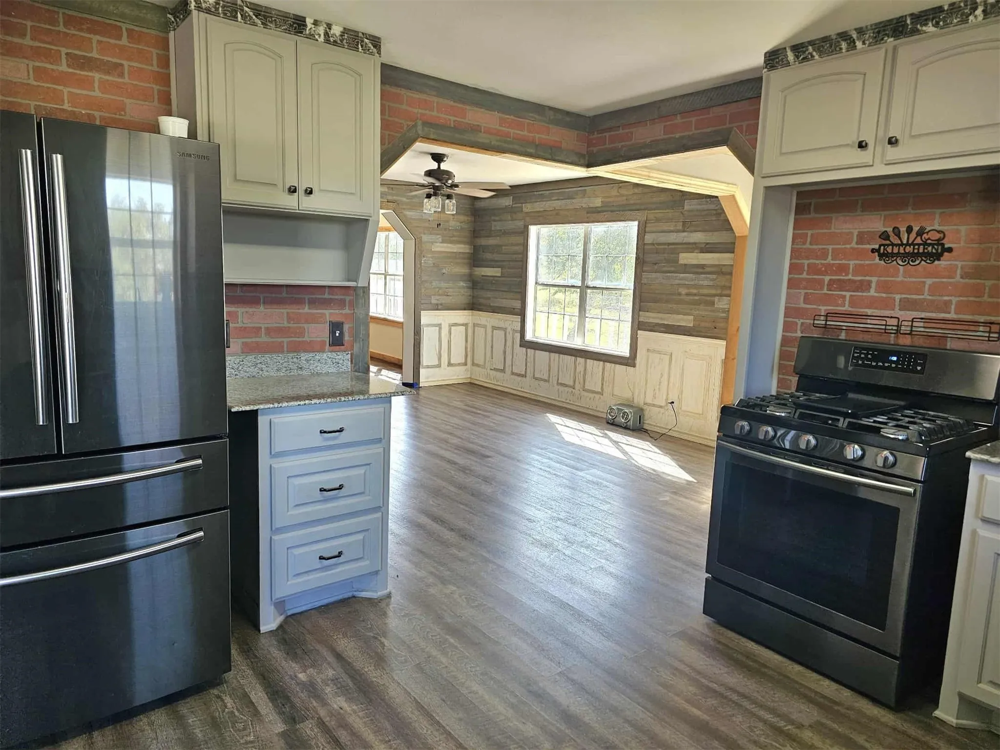 Kitchen with stainless steel appliances, dark wood-style flooring, light stone counters, a ceiling fan, and a wainscoted wall