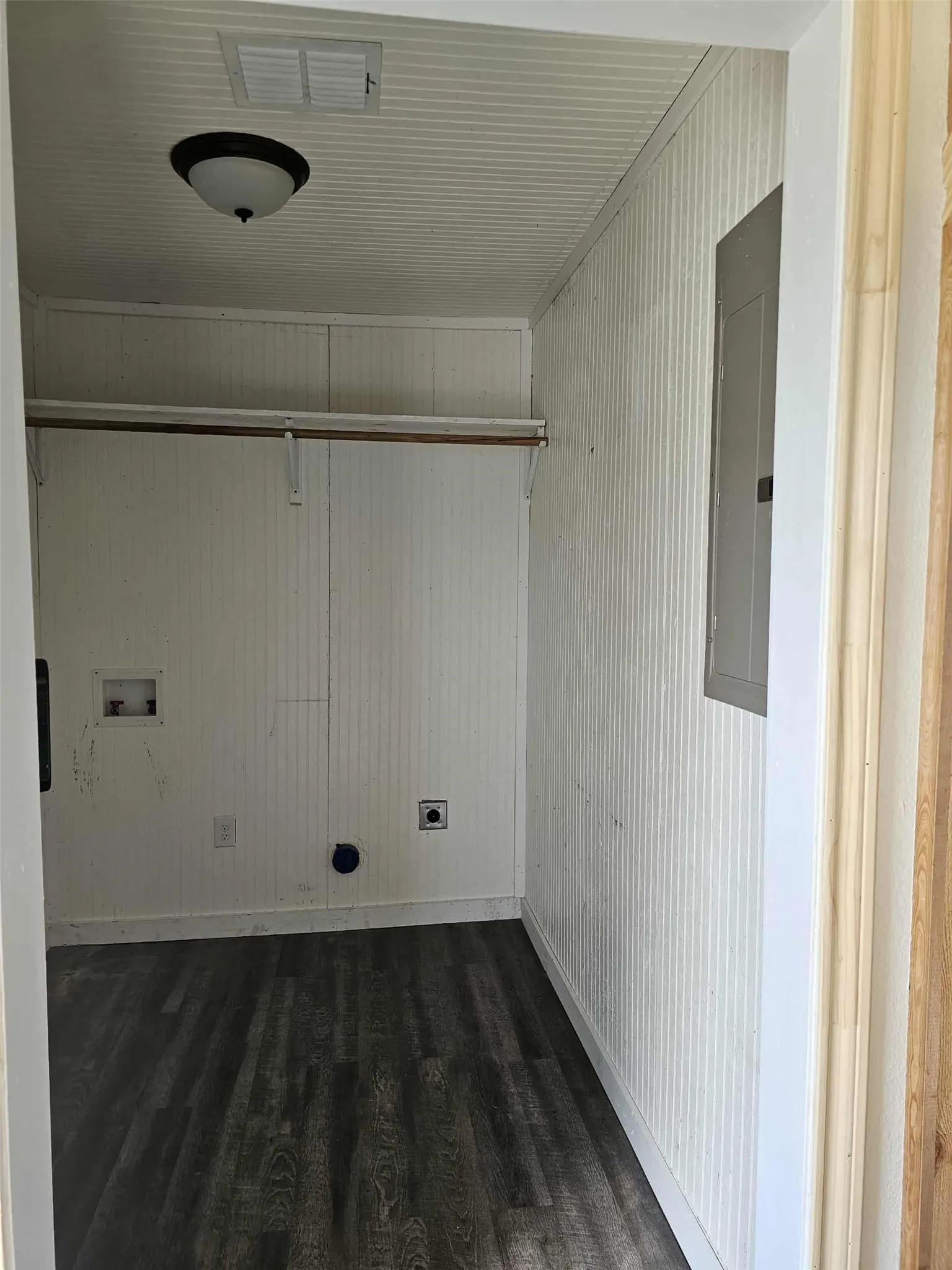 Laundry room with dark wood-style flooring, wood walls, washer hookup, and electric panel