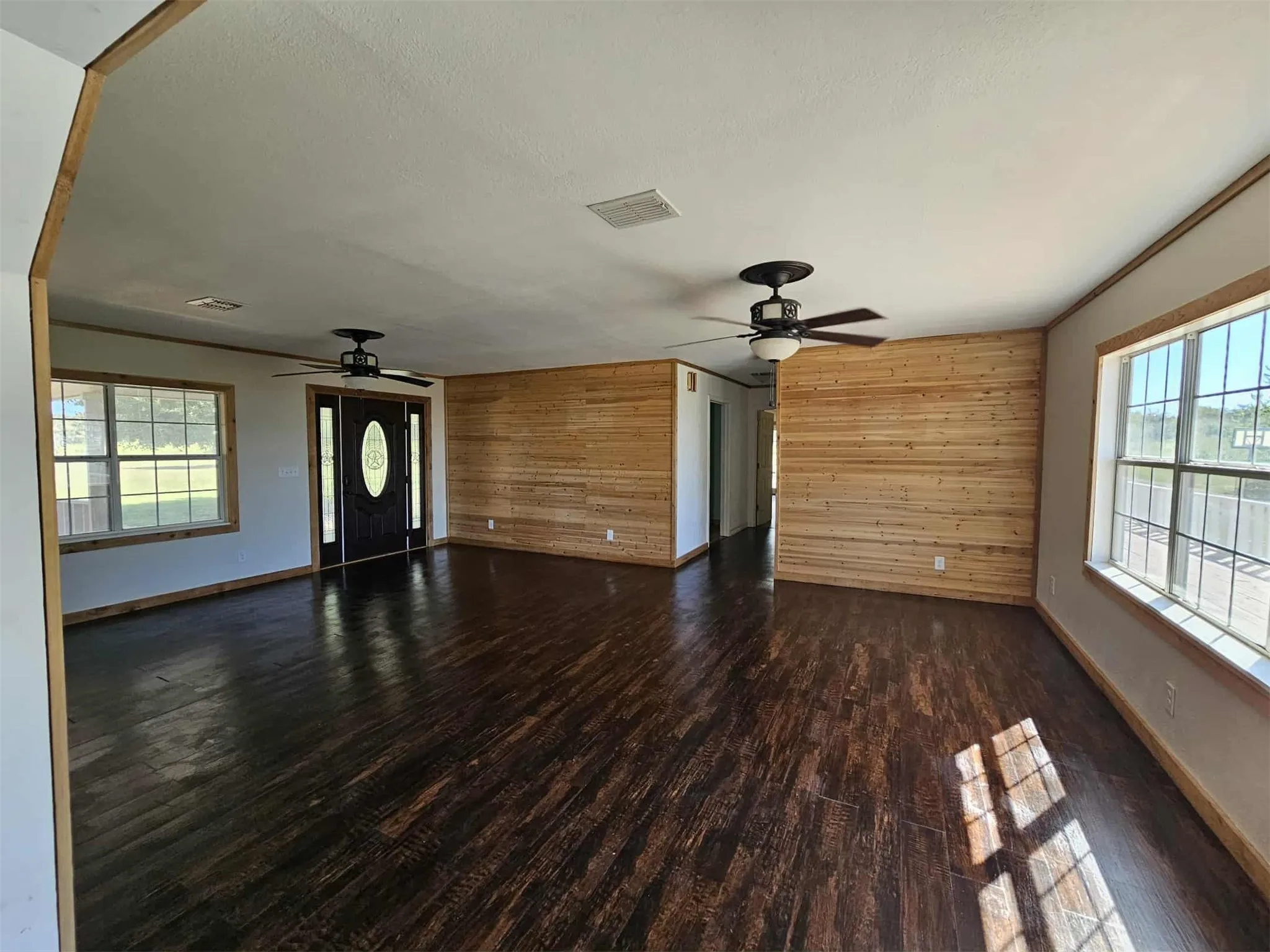 Unfurnished living room featuring wooden walls, dark wood finished floors, and a ceiling fan
