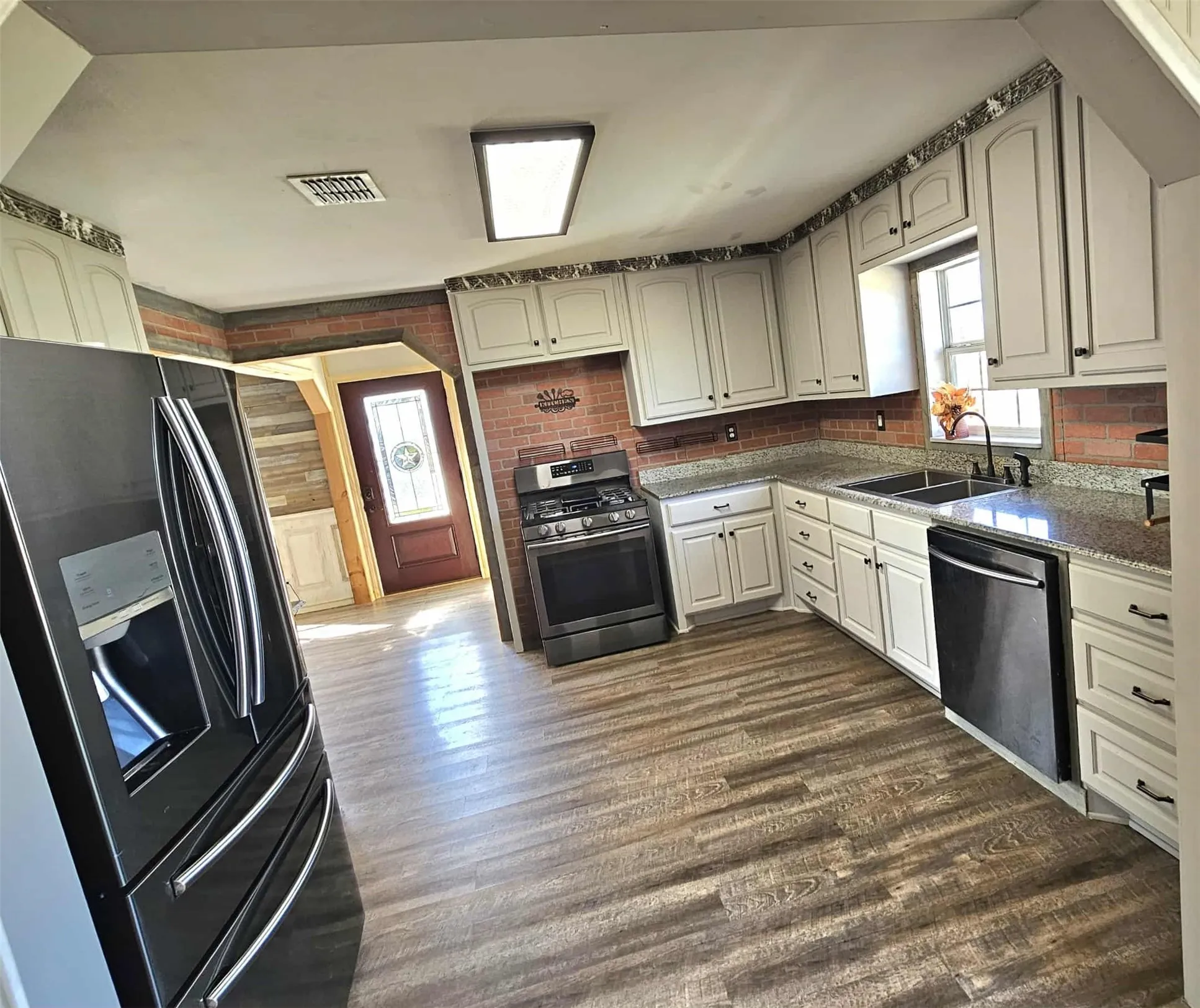 Kitchen with black fridge, dark wood-style flooring, light stone countertops, stainless steel range with gas stovetop, and dishwasher