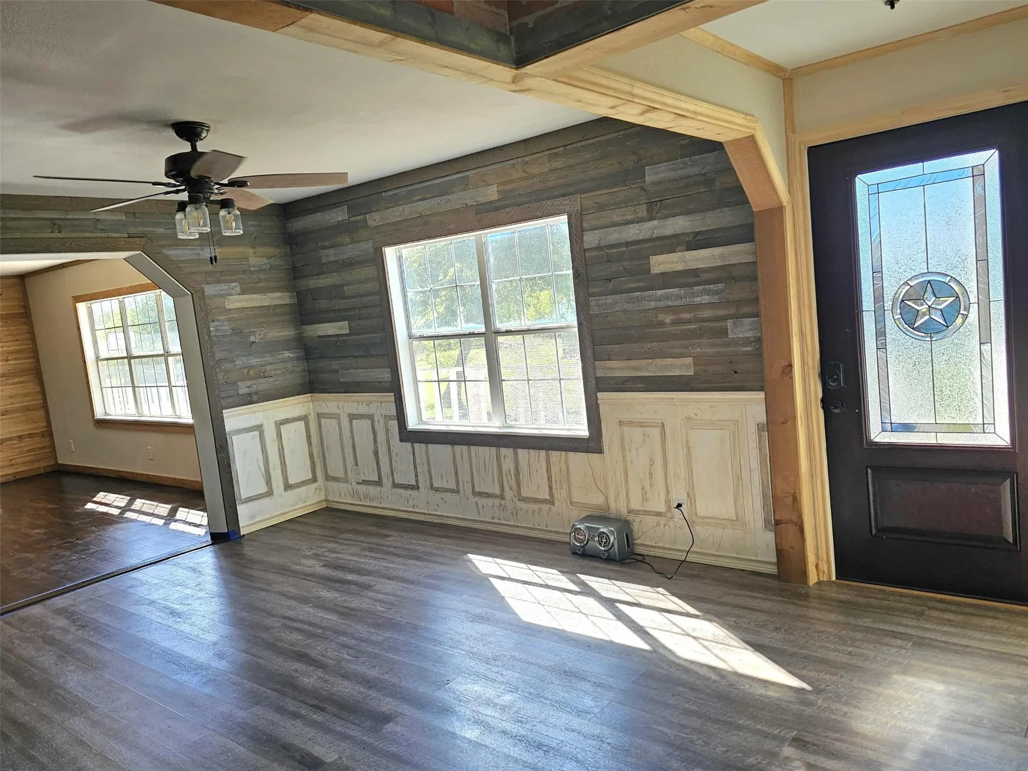 Rear entrance with dark wood-style flooring, wooden walls, arched walkways, wainscoting, and a ceiling fan