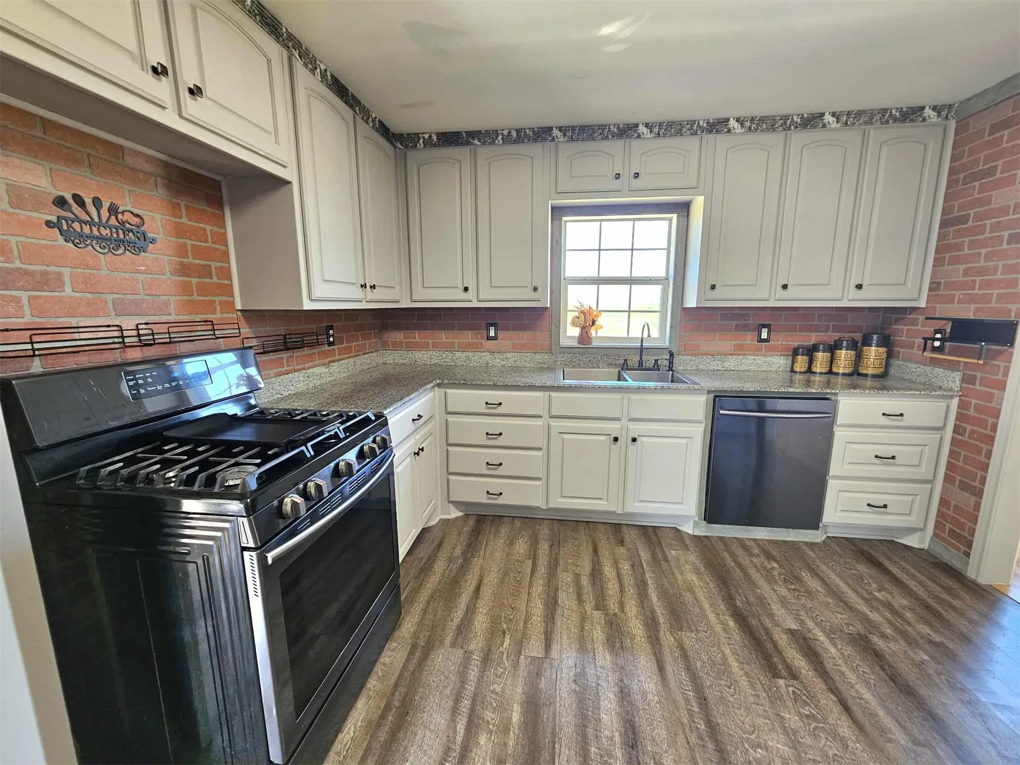 Kitchen with stainless steel appliances, light stone countertops, dark wood-style floors, and brick wall